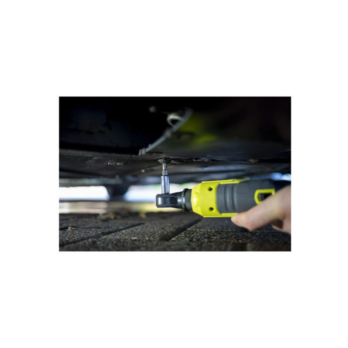 Eine Person zieht mit einer gelb-grauen elektrischen Ratsche eine Schraube unter einem Auto fest.