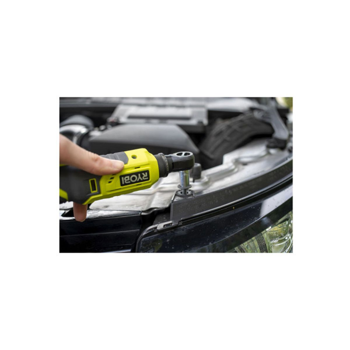 Eine Person benutzt eine gelbe Ryobi-Akkuratsche, um eine Schraube im Motorraum eines Autos anzuziehen.