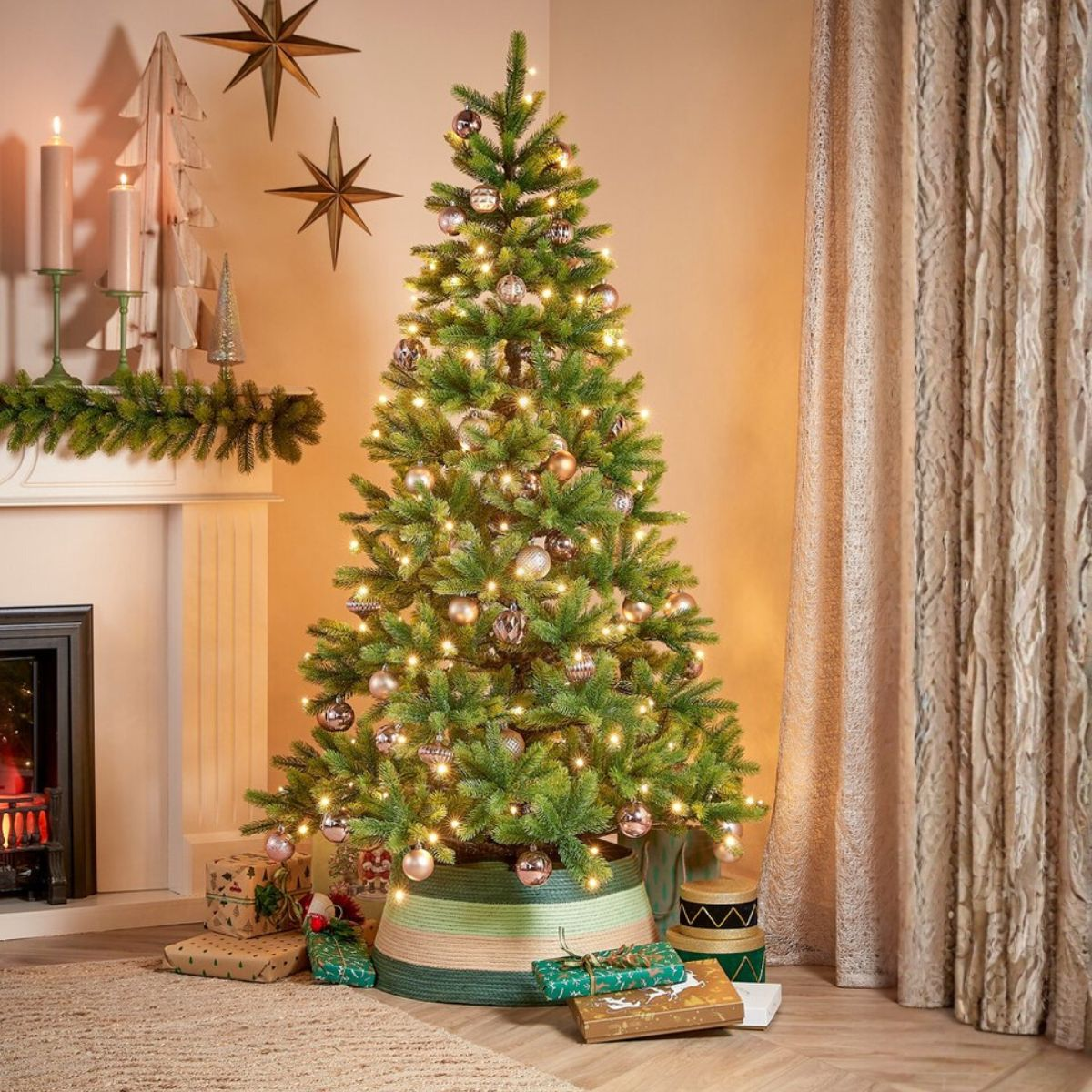 An illuminated Christmas tree stands in a living room with a fireplace, wrapped gifts below, and stars on the wall.