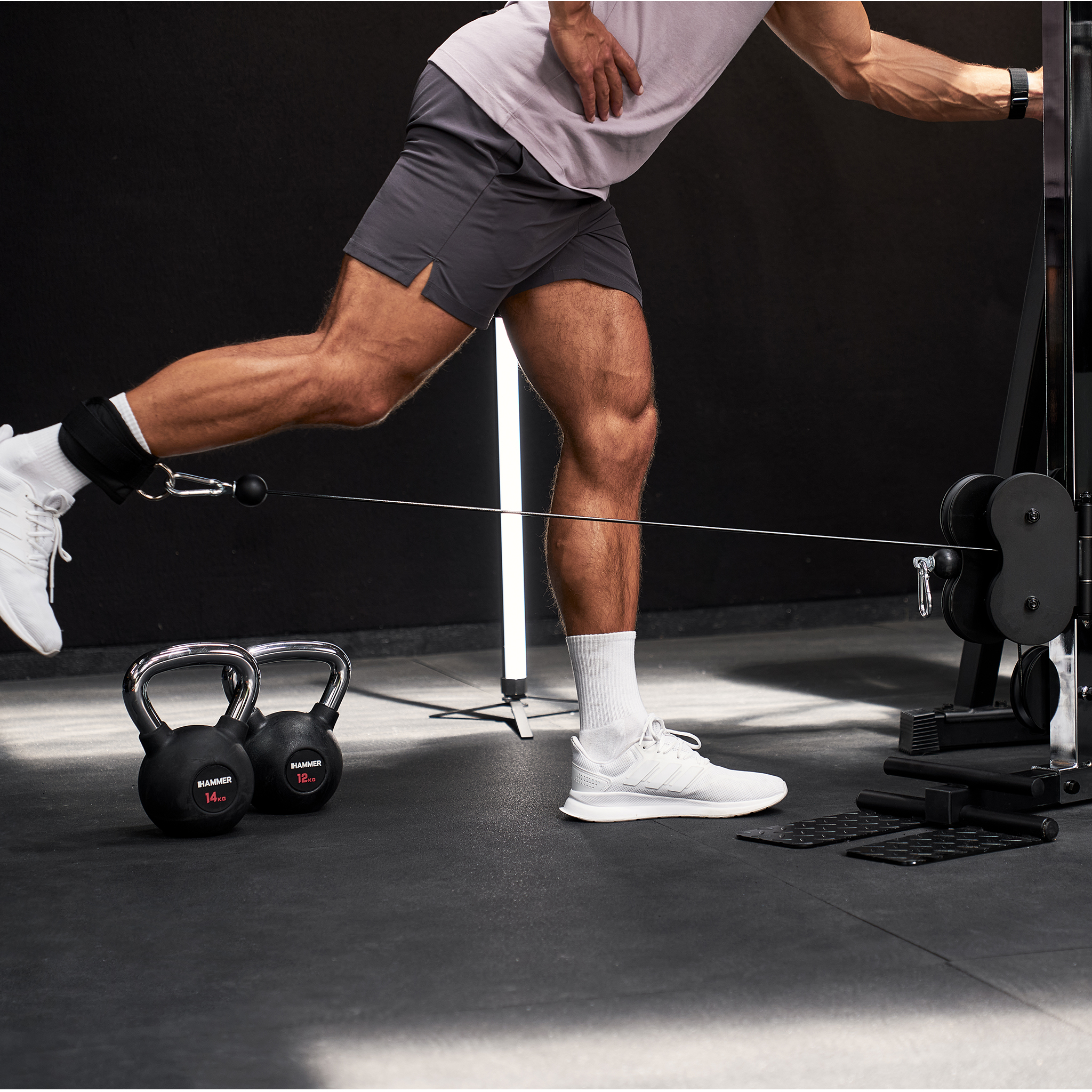 Ein Mann im Fitnessstudio macht Kabel-Kickbacks, während zwei Kettlebells in der Nähe stehen.