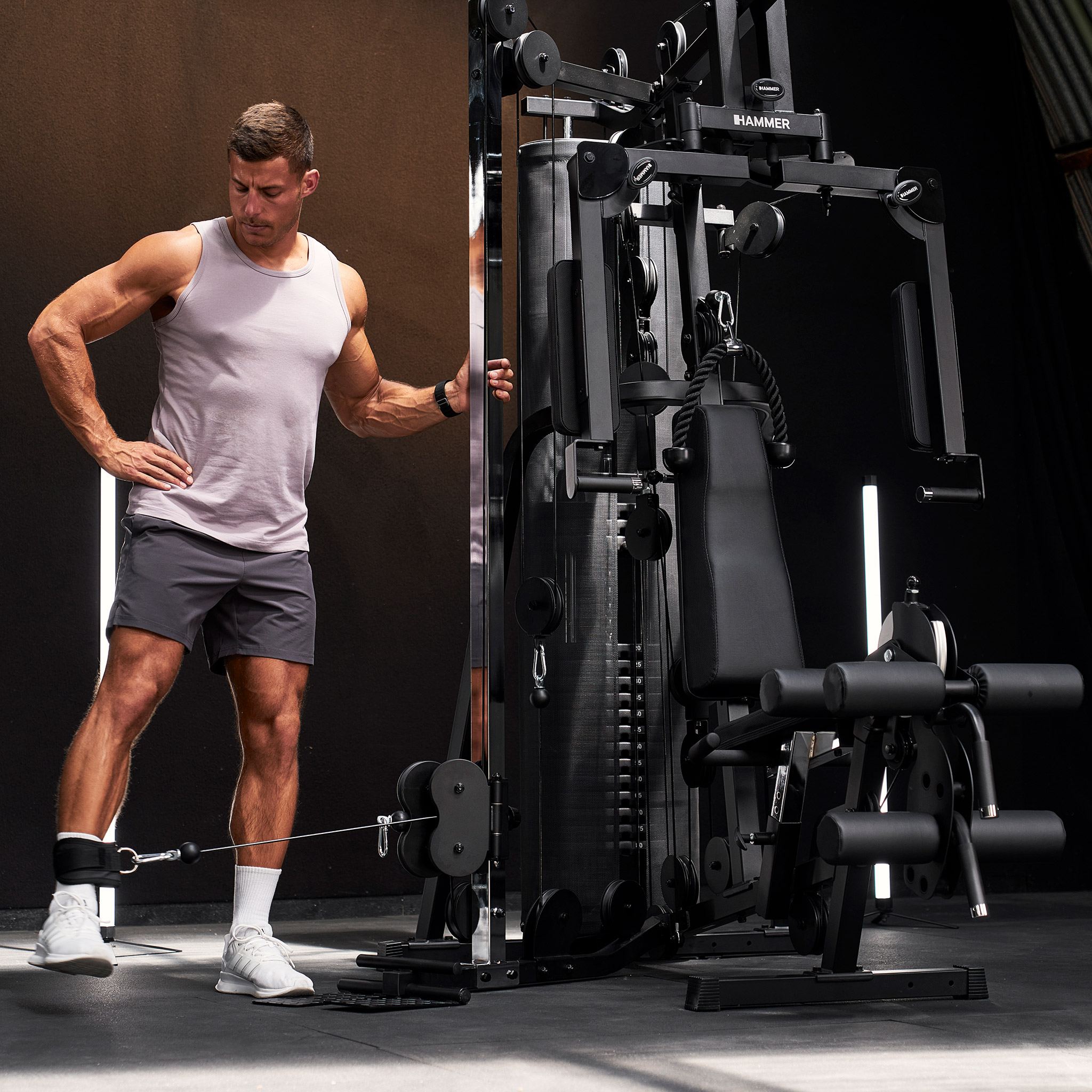 Muskulöser Mann in Sportkleidung trainiert Beine an einer schwarzen Fitnessstation im Studio.