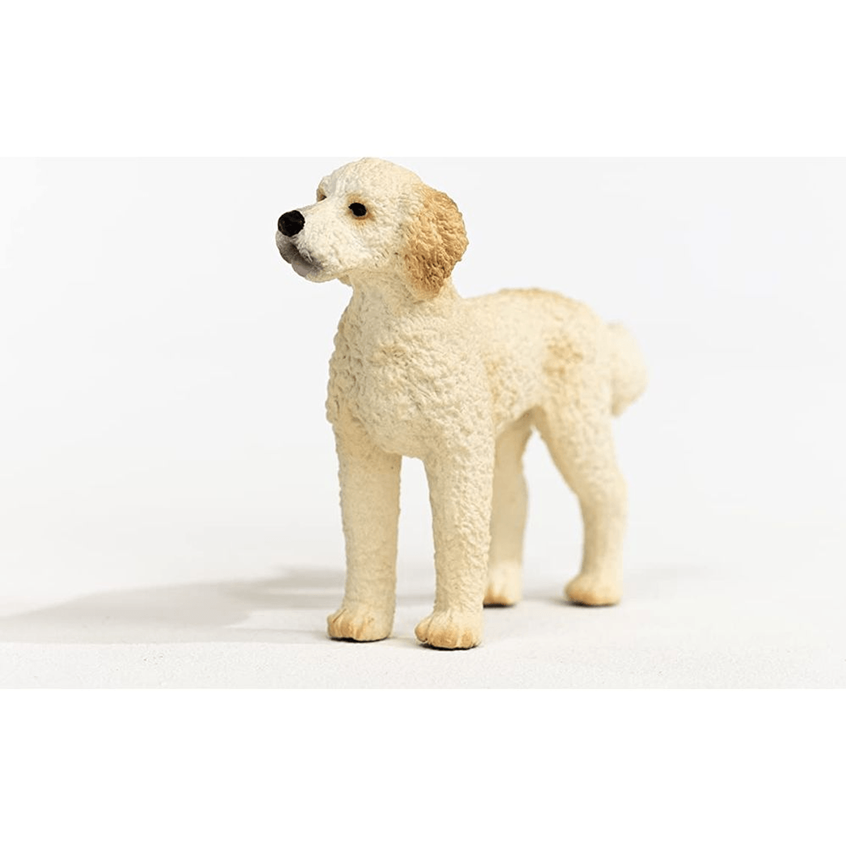 Una piccola statuetta di cane color crema con pelliccia riccia su sfondo bianco.