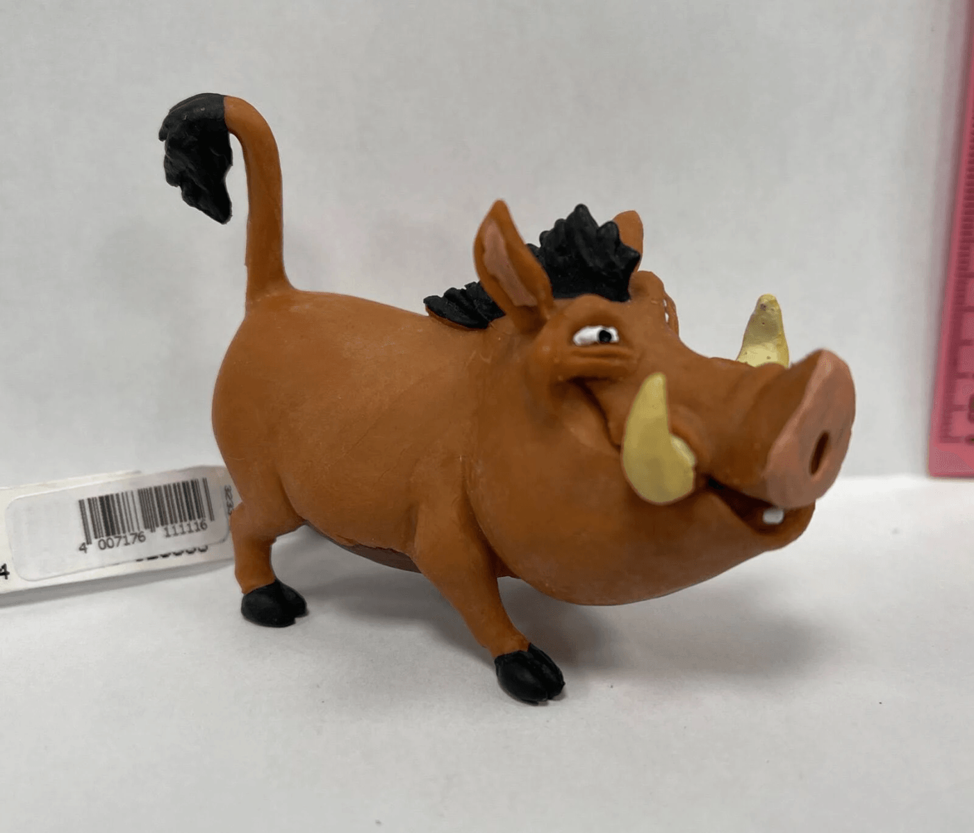 Eine Pumbaa-Kunststofffigur aus Der König der Löwen steht auf weißer Oberfläche mit Barcode.