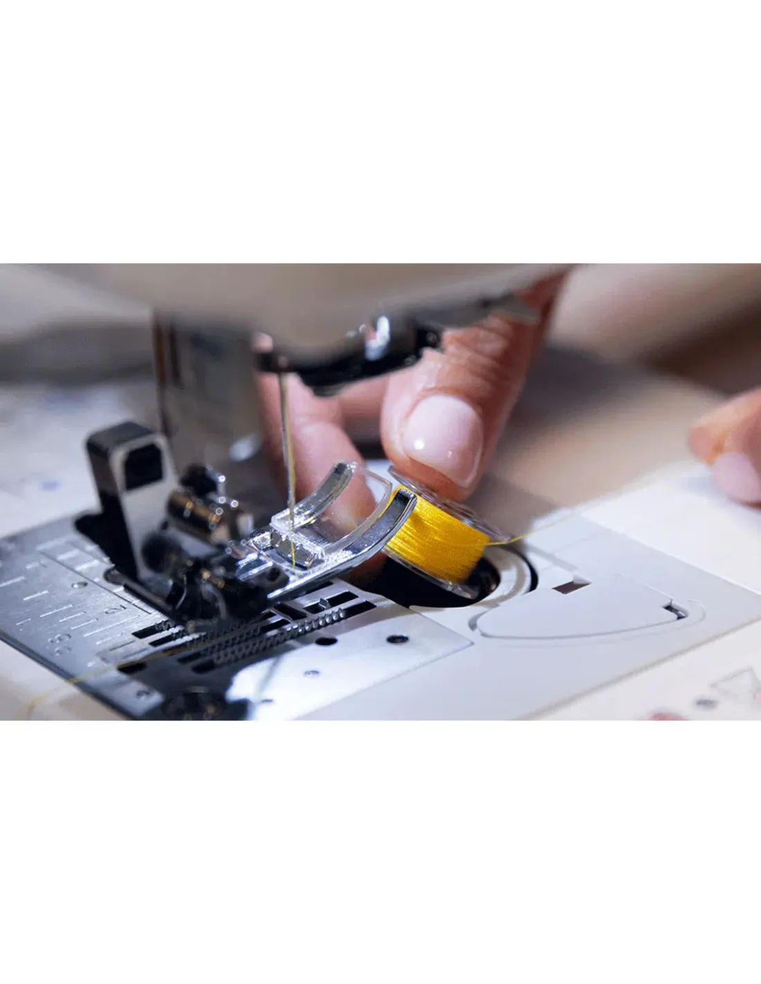 A hand places a spool of yellow thread into the bobbin case of a sewing machine.