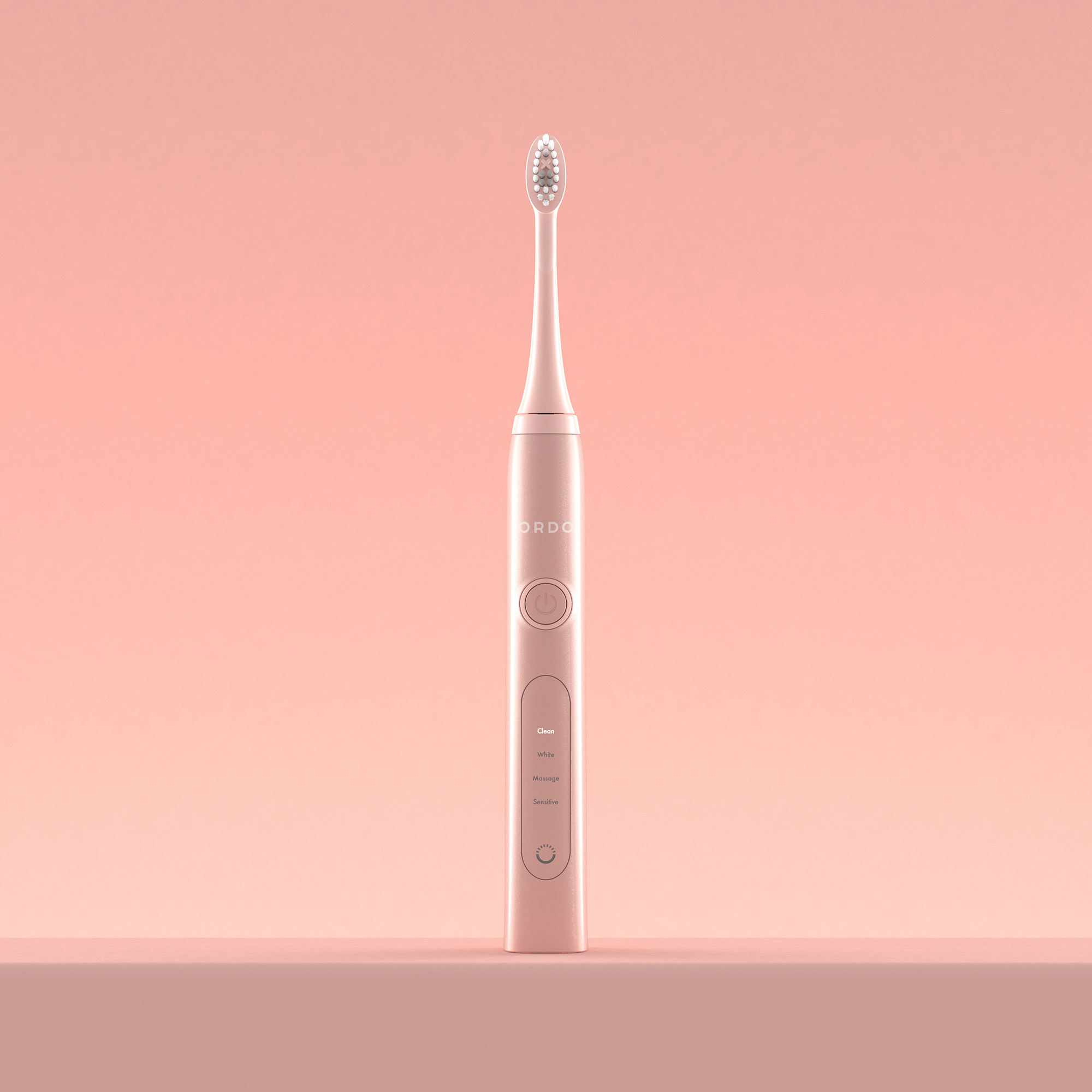 Uno spazzolino elettrico rosa è posizionato verticalmente su uno sfondo rosa uniforme, sopra un ripiano coordinato.