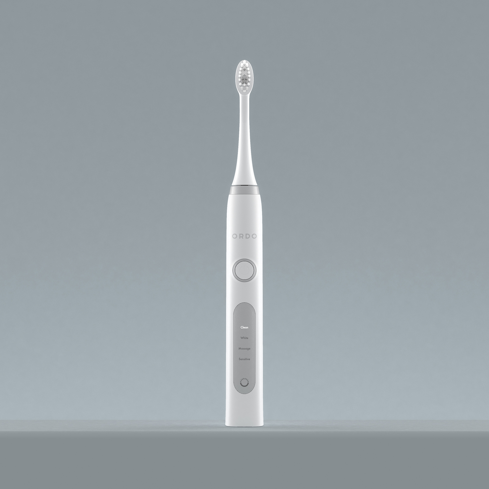 Un cepillo de dientes eléctrico Ordo blanco se encuentra en posición vertical sobre un fondo gris liso.