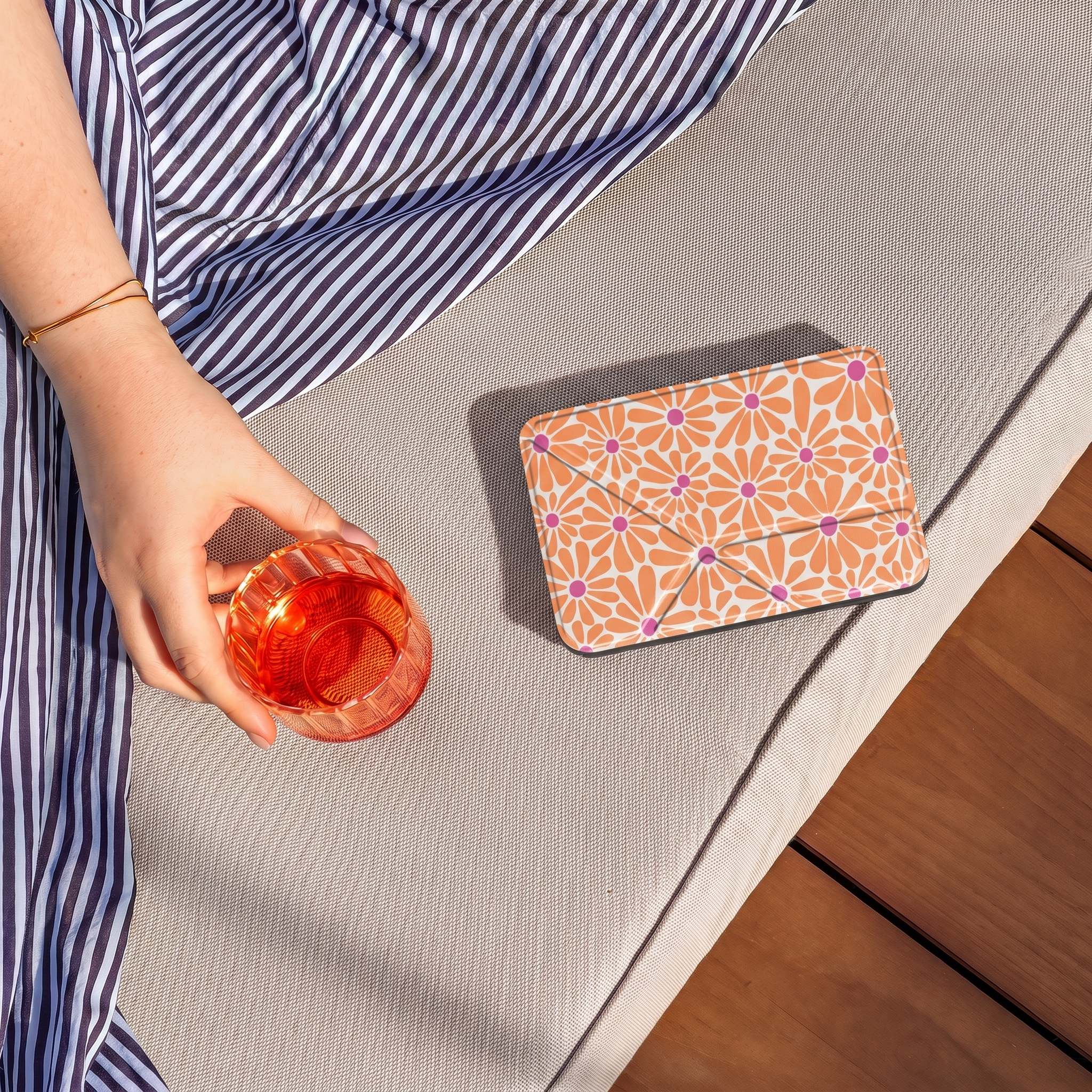 Personne en robe rayée tient un verre rouge près d'un étui fleuri sur un transat.