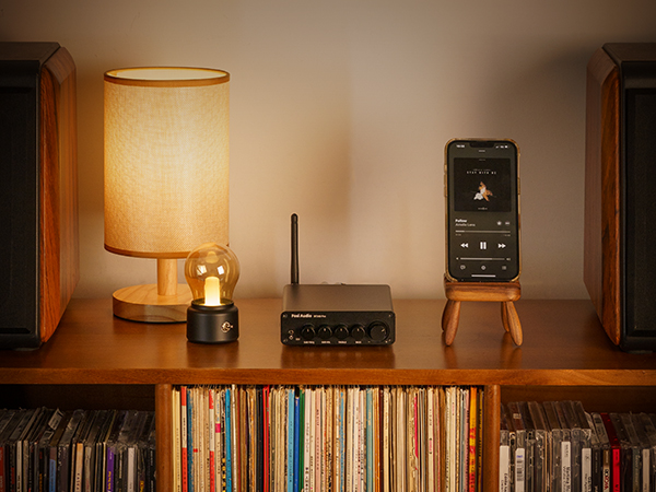 Wzmacniacz audio, lampa i smartfon na drewnianej półce nad półkami wypełnionymi płytami winylowymi.