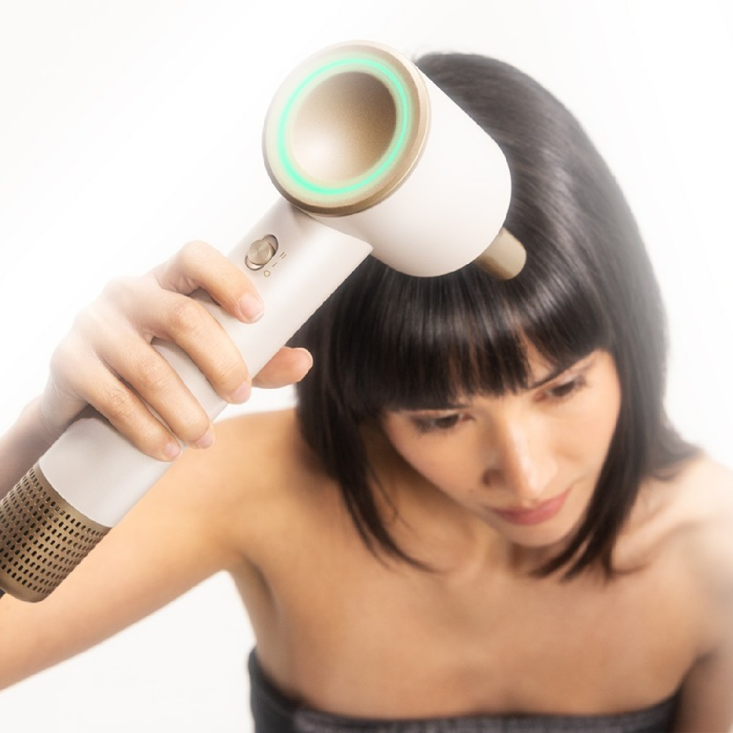 Una mujer sostiene un secador de pelo moderno blanco y dorado con un anillo verde brillante.