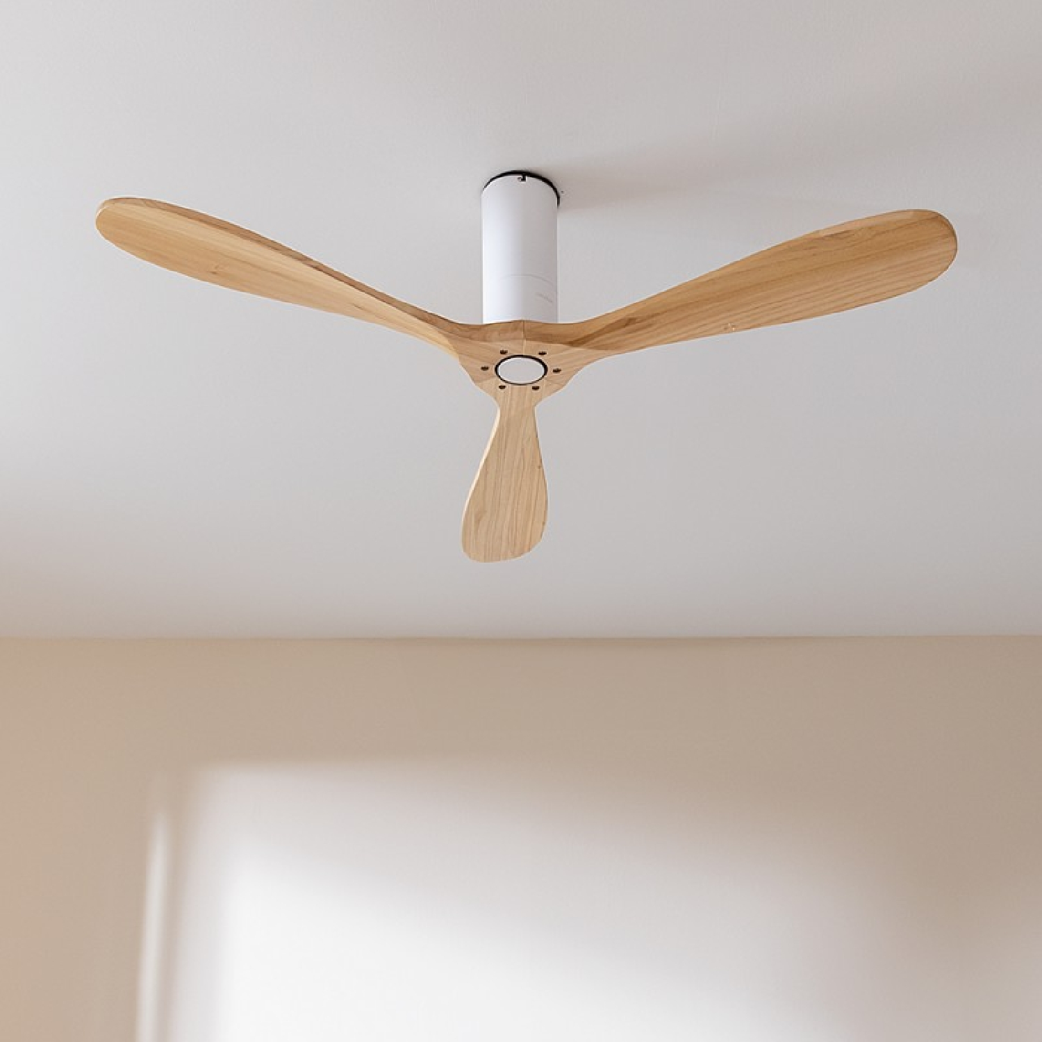 Un ventilatore da soffitto in legno a tre pale montato su un soffitto bianco.