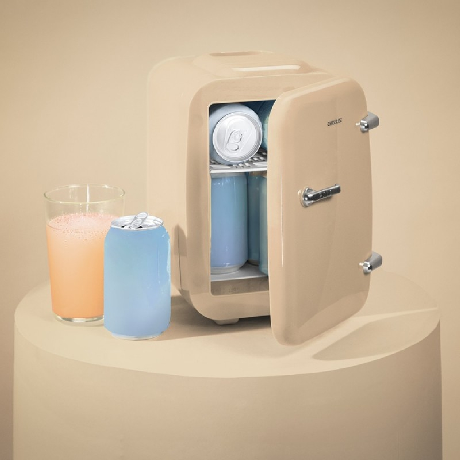 Mini frigo beige con porta aperta, lattine blu e un bicchiere di succo su un piedistallo rotondo.