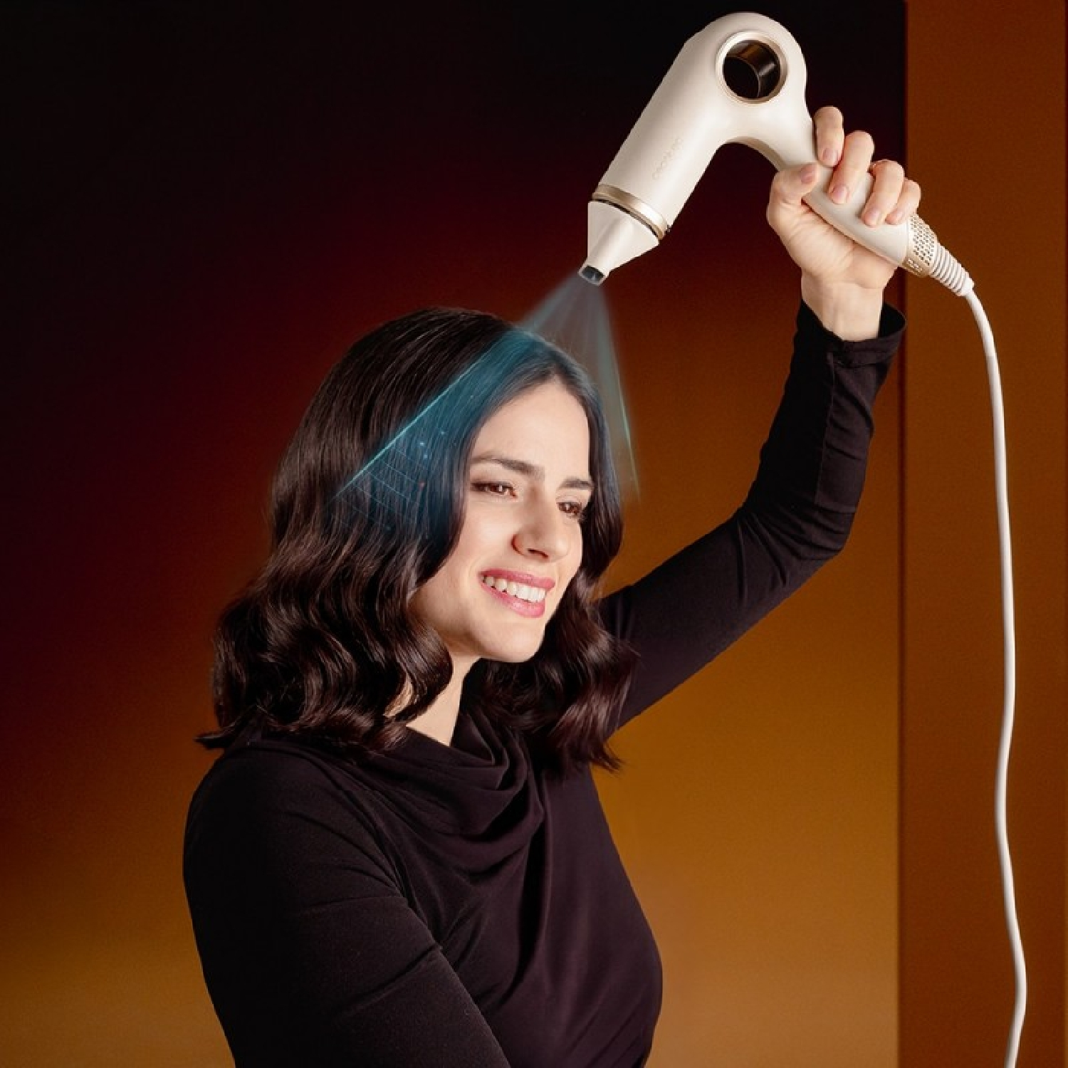 Una donna sorridente in nero usa un phon beige, dirigendo un flusso d'aria blu sui suoi capelli scuri.