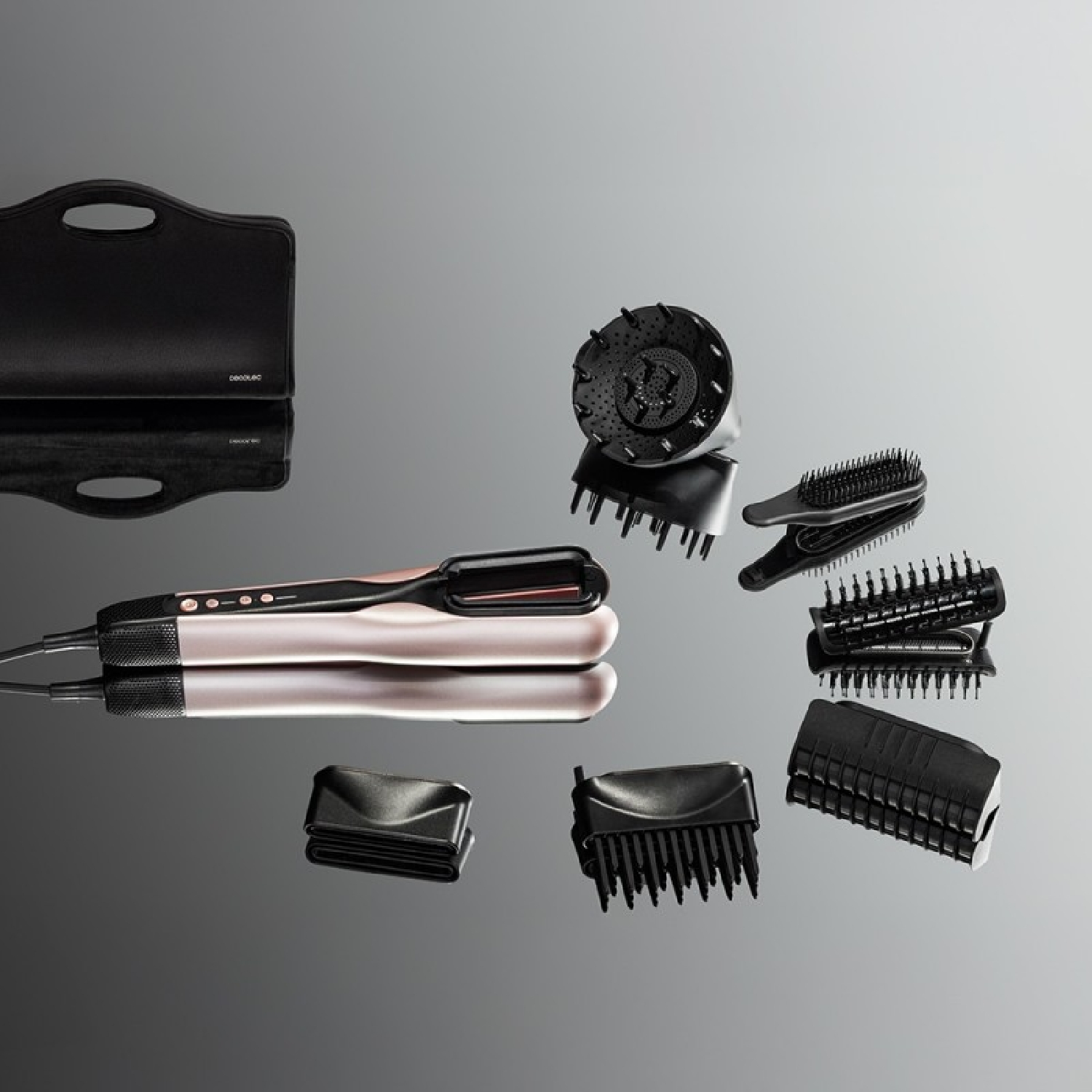 Una herramienta de peinado rosa y negro con varios accesorios y un estuche sobre una superficie gris.