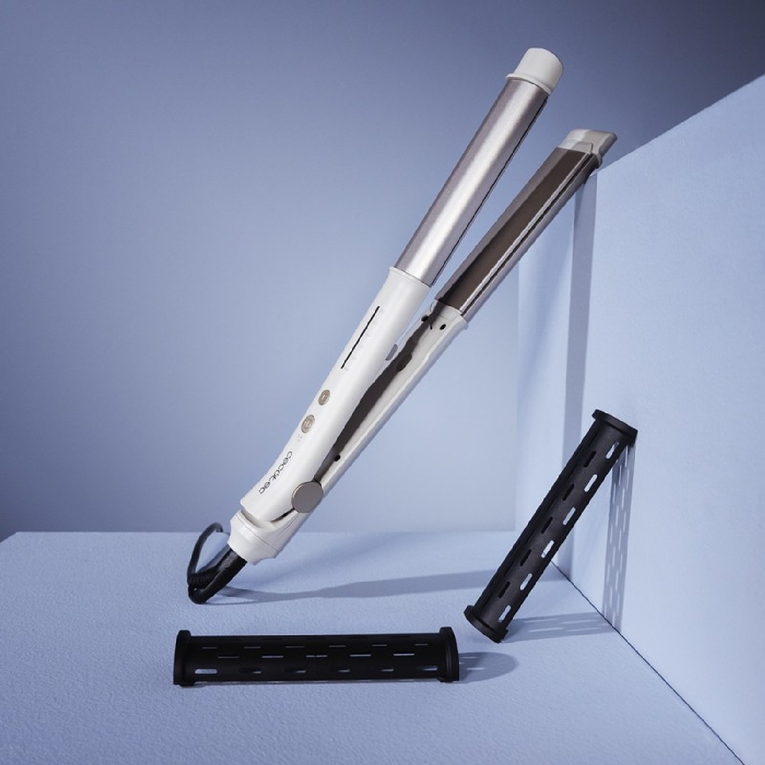 Styler per capelli bianco e argento con due accessori neri su superficie azzurra.