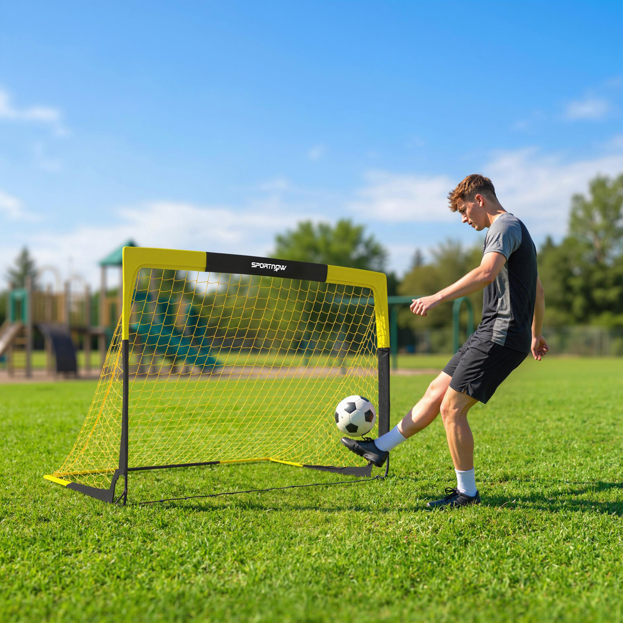 Un niño patea un balón de fútbol hacia una portería amarilla en un campo verde.