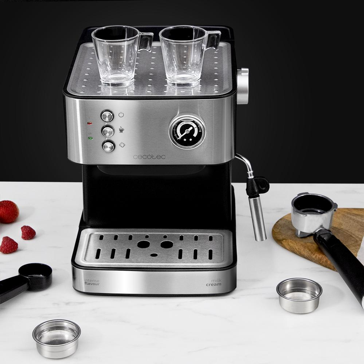 Una macchina da caffè espresso argento e nera su un bancone con due tazze sopra e accessori.
