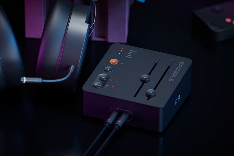 Un mixer audio nero con cursori, pulsanti e cavi collegati, posizionato su una superficie scura accanto alle cuffie.