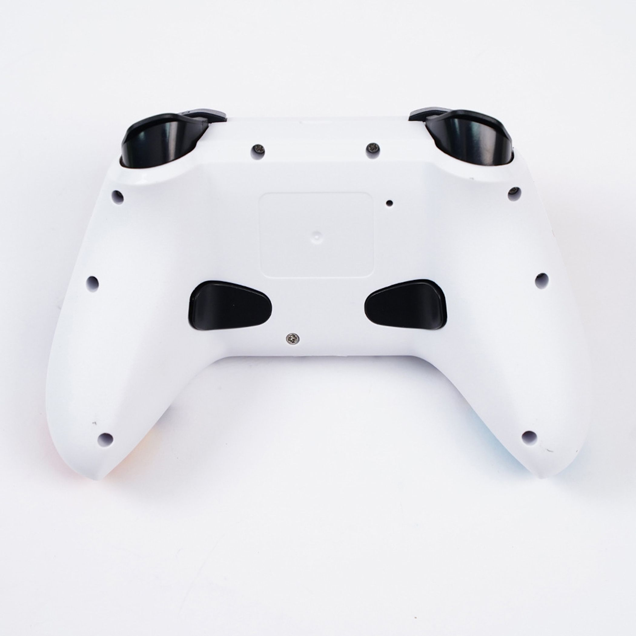 Rückseite eines weißen Gamecontrollers mit schwarzen Tasten und Schrauben auf hellem Hintergrund.