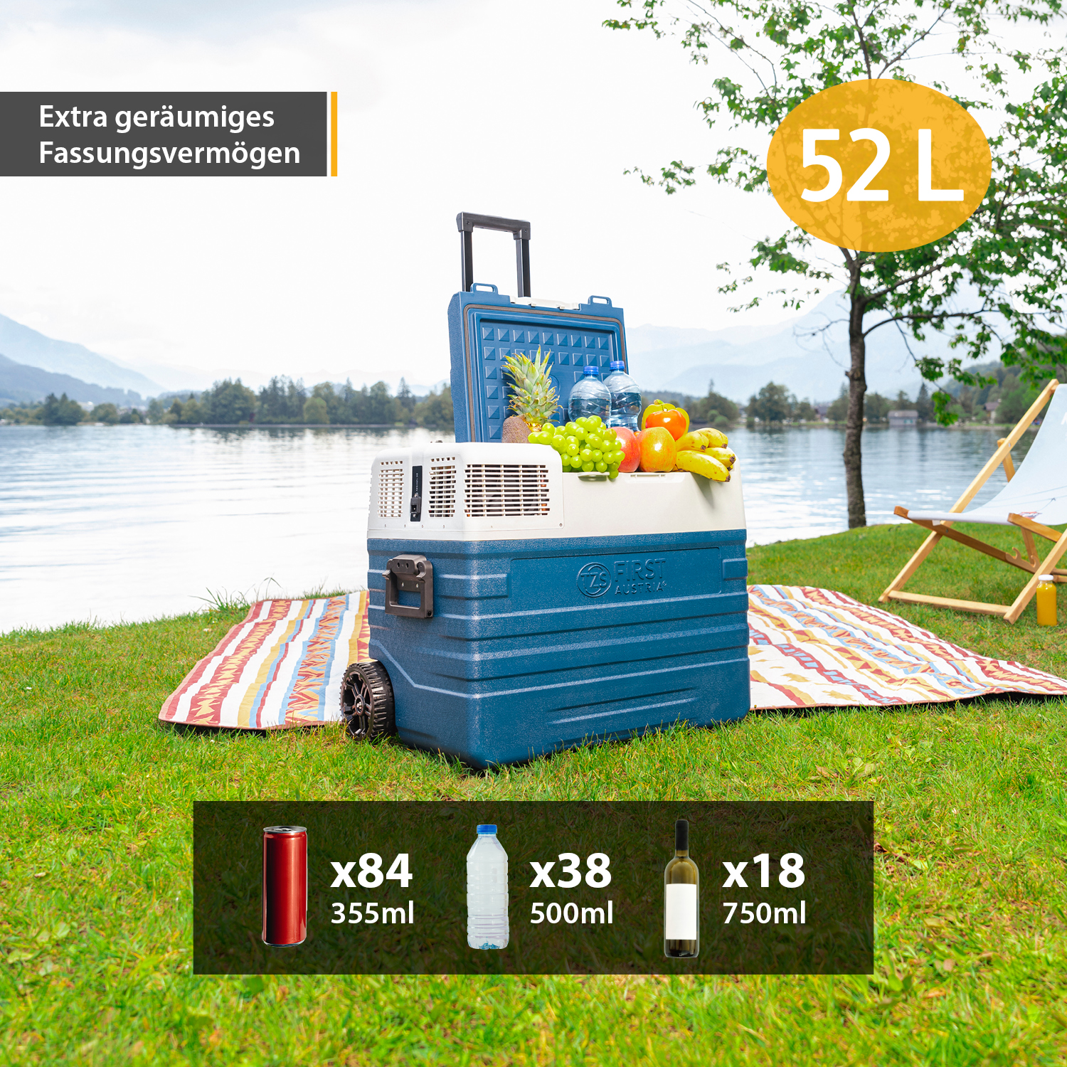 Blaue 52L Kühlbox mit Rollen und gefüllt mit frischem Obst, stehend auf einer Picknickdecke am See.