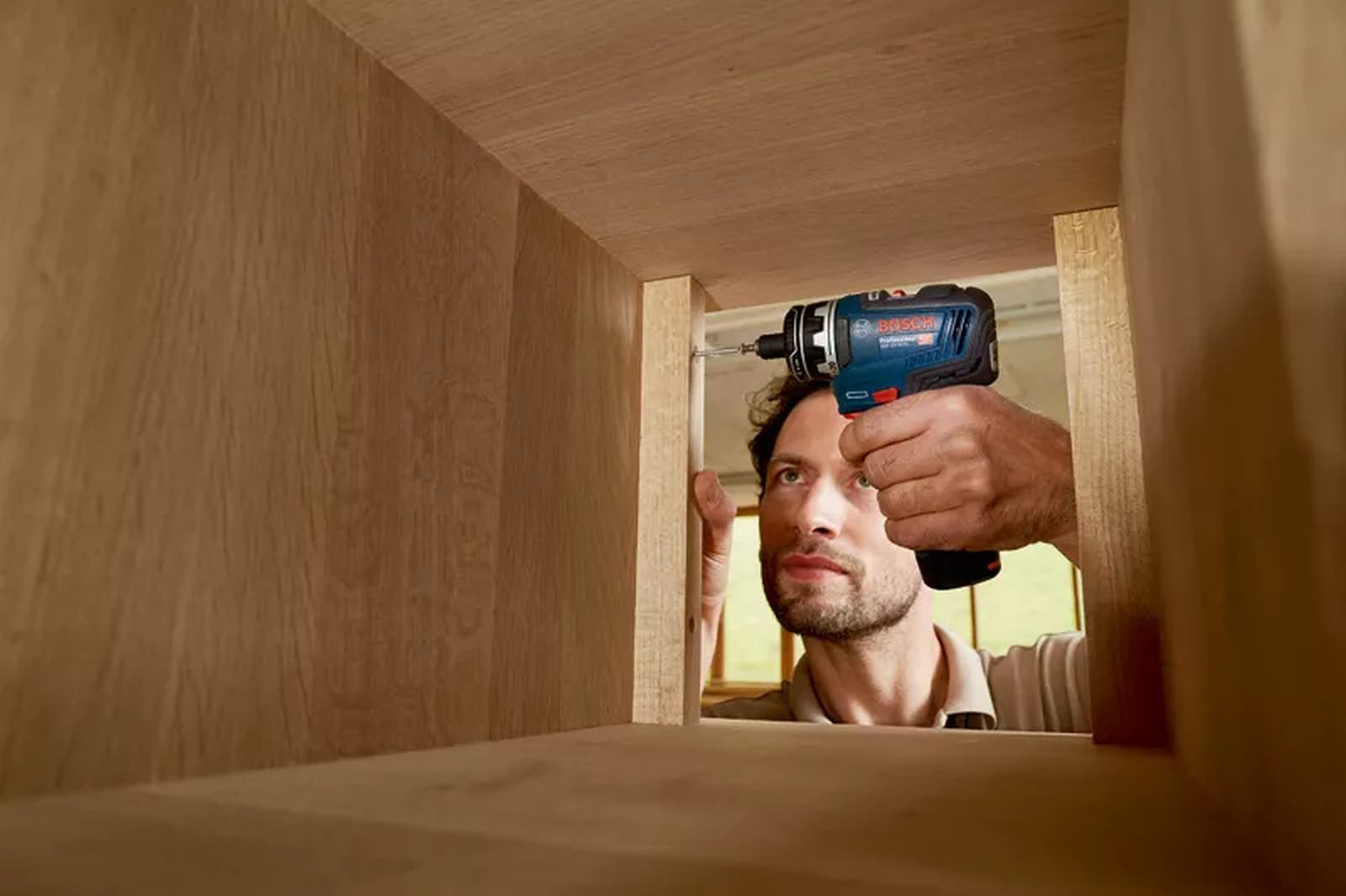 Un uomo usa un avvitatore a batteria Bosch blu per avvitare parti in legno.