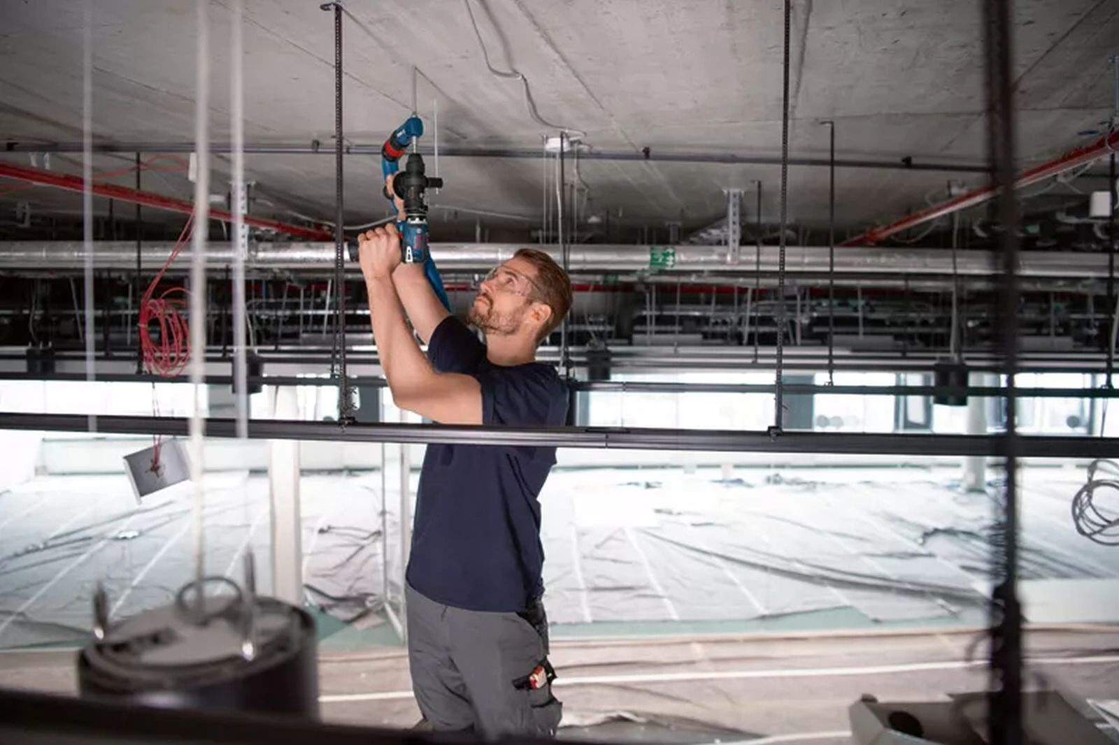 Un uomo con occhiali protettivi usa un martello perforatore blu per forare un soffitto.