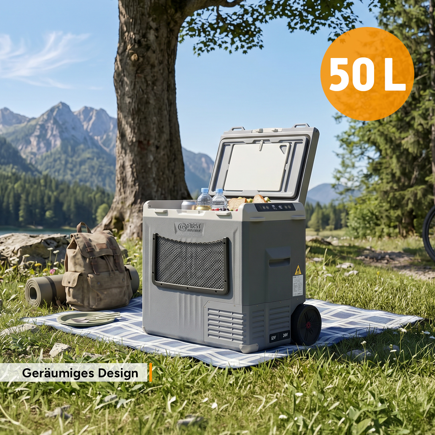 Eine graue 50L Kühlbox steht auf einer Picknickdecke im Freien, im Hintergrund Berge und Bäume.