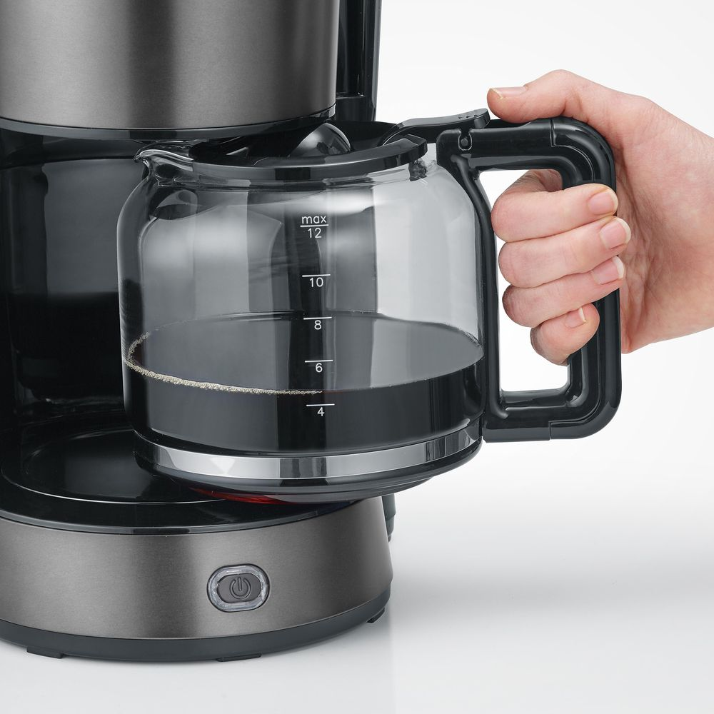 Eine Hand hält die Glaskanne einer Kaffeemaschine gefüllt mit schwarzem Kaffee.