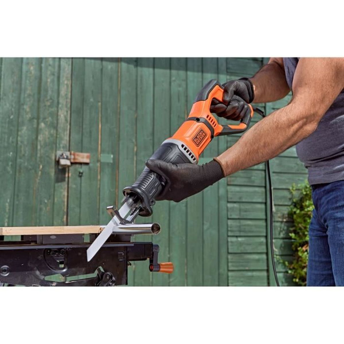 Eine Person mit schwarzen Handschuhen schneidet draußen mit einer orangen Säge ein Metallrohr.