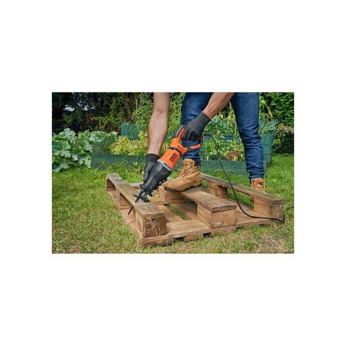 Eine Person schneidet im Garten eine Holzpalette mit einer orange-schwarzen Säbelsäge.