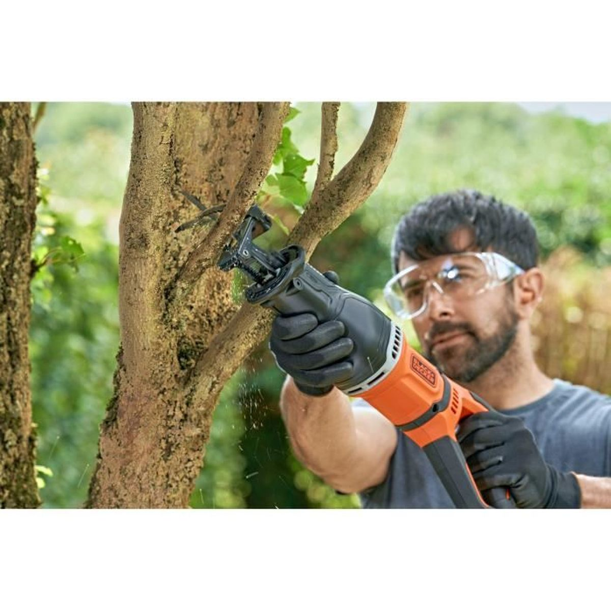 Ein Mann mit Schutzbrille und Handschuhen schneidet mit einer elektrischen Säbelsäge einen Ast ab.