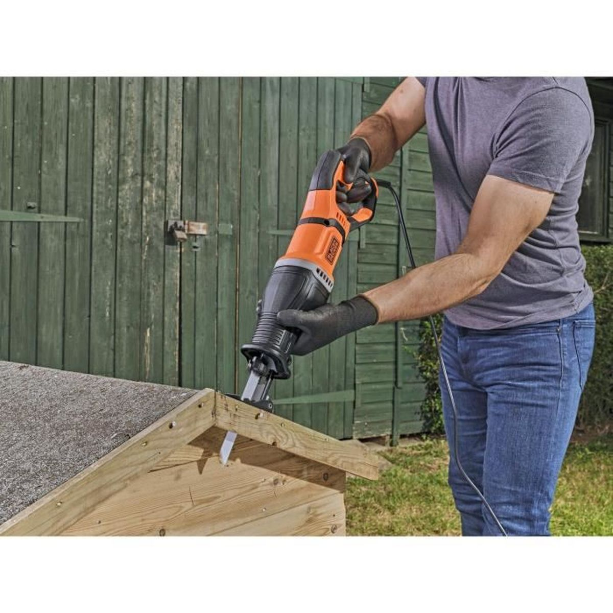 Ein Mann mit Handschuhen schneidet mit einer elektrischen Säge Holz an einem kleinen Schuppen.