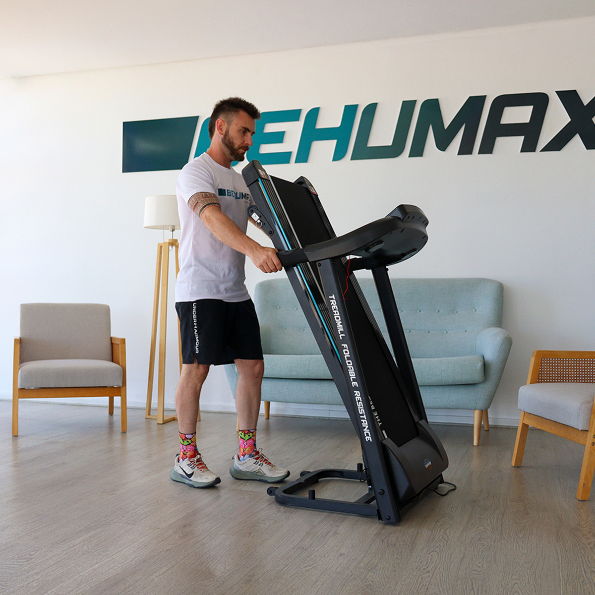 Un hombre levanta una caminadora plegable en una habitación luminosa.