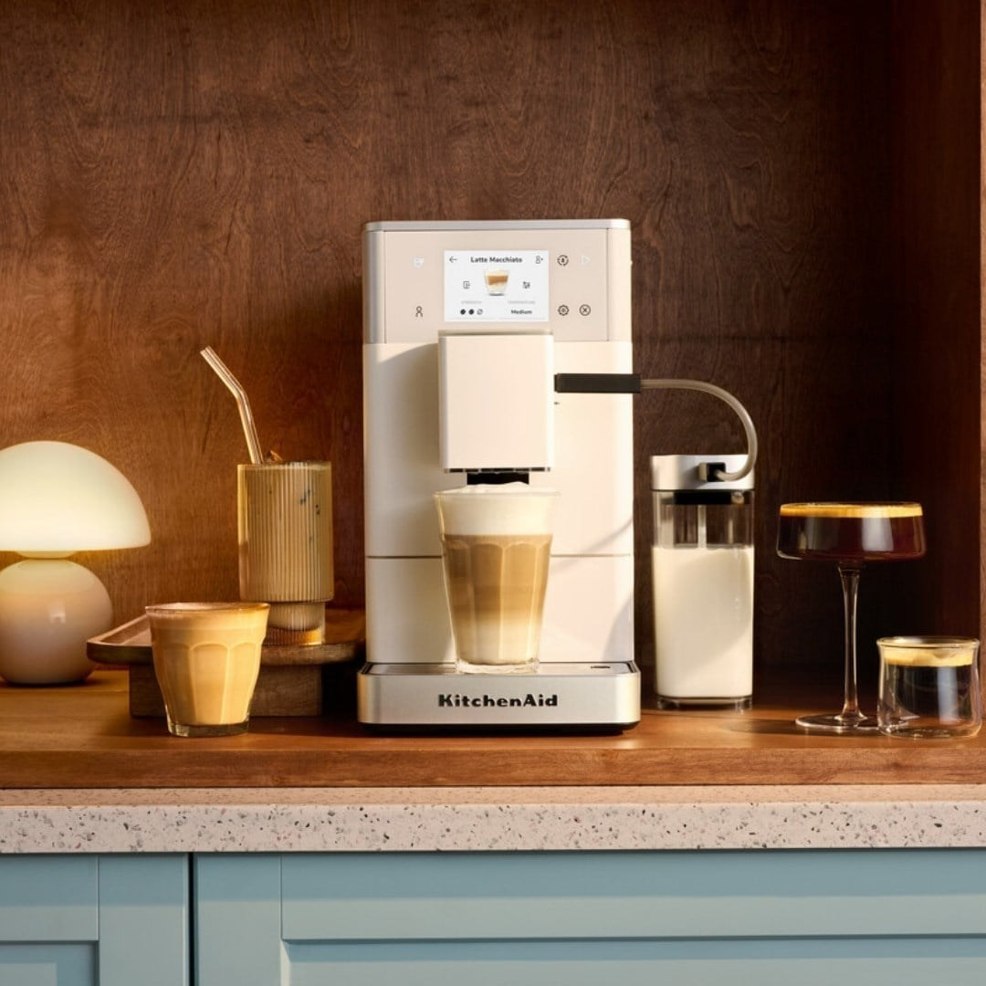 Bir tezgah üzerinde beyaz KitchenAid kahve makinesi, çeşitli kahve içecekleri ve lamba.