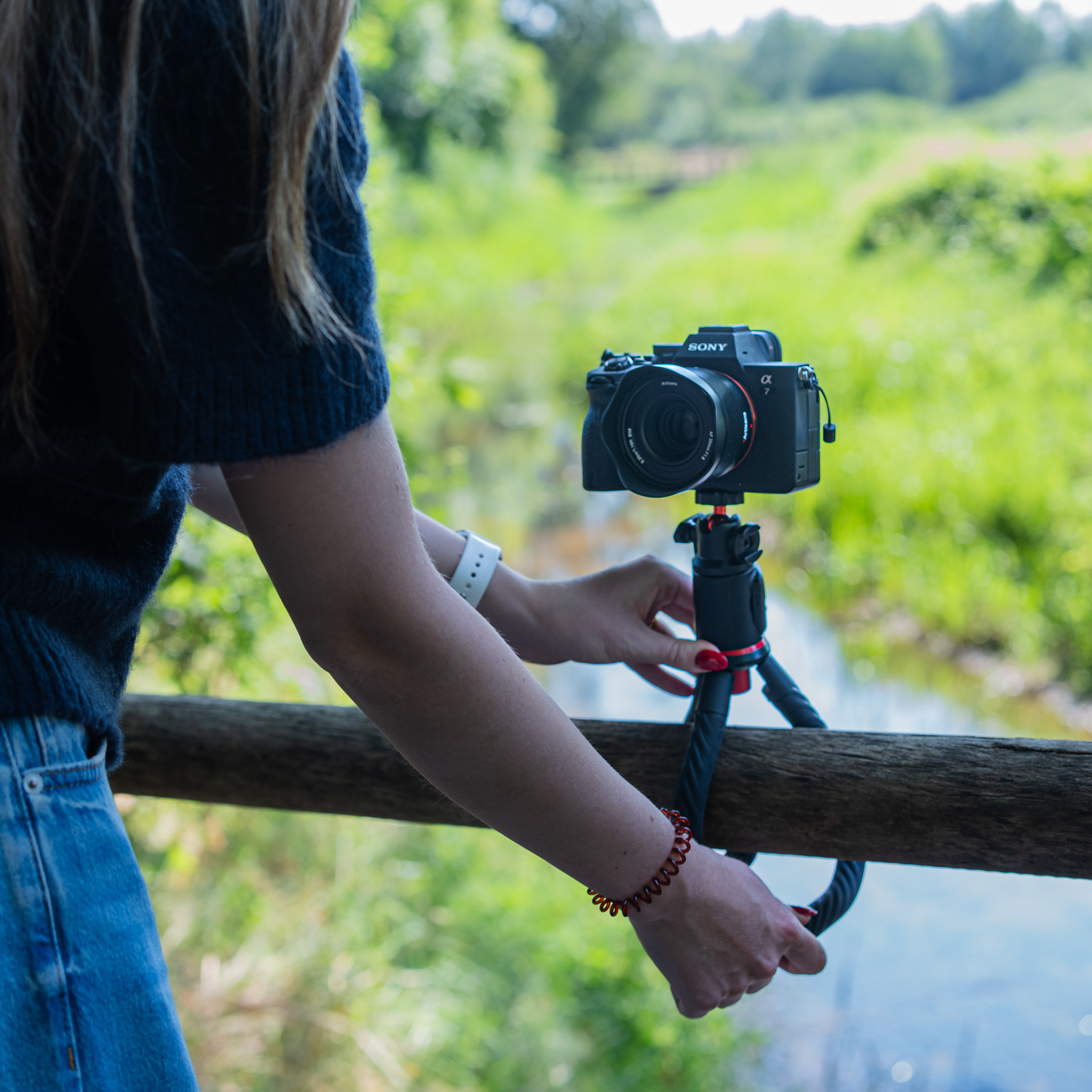 A woman attaches a Sony camera to a flexible tripod on a wooden rail outdoors.