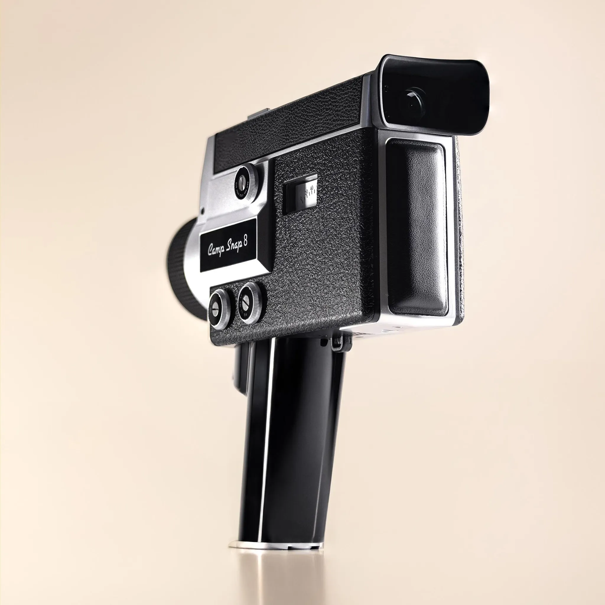 Eine vintage schwarze und silberne Super-8-Schmalfilmkamera steht aufrecht auf einer hellen Unterlage vor hellem Hintergrund.