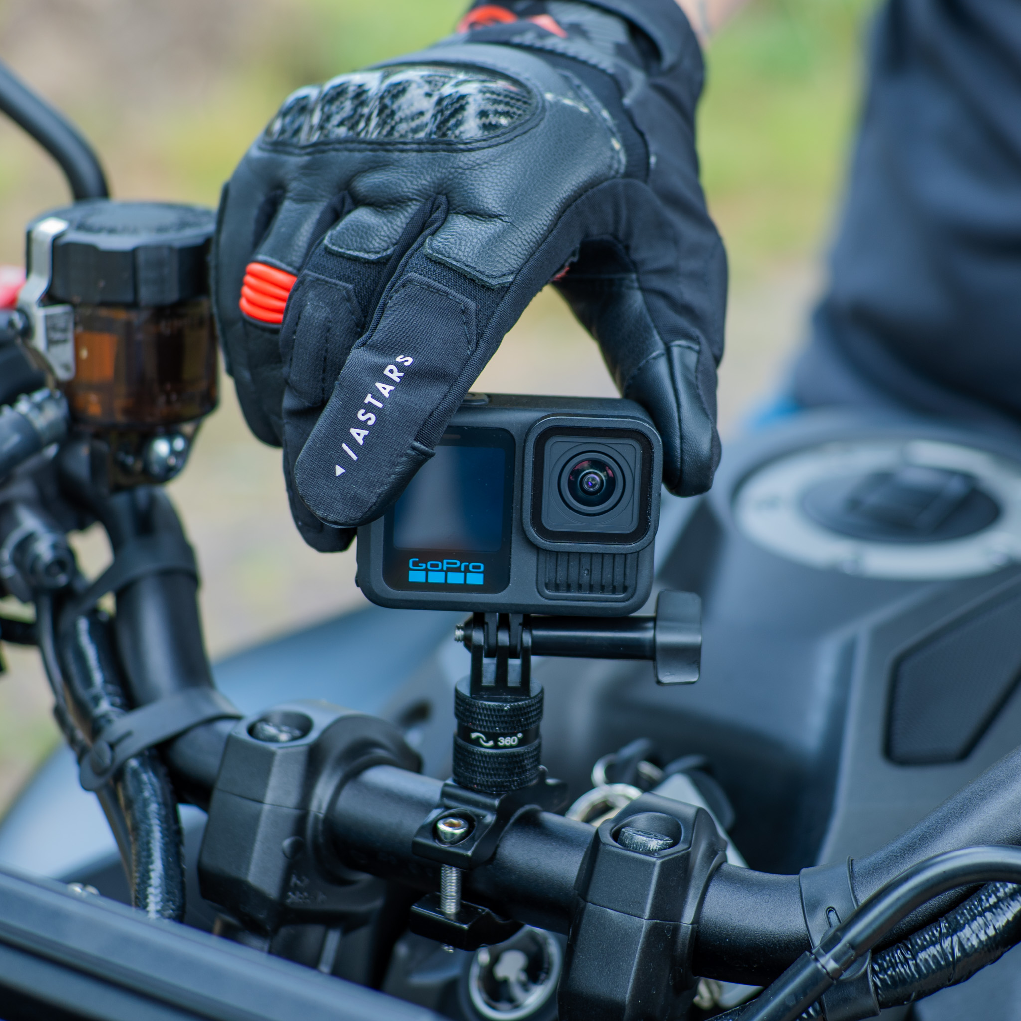 Een gehandscoende hand monteert een GoPro-camera op een motorstuur.