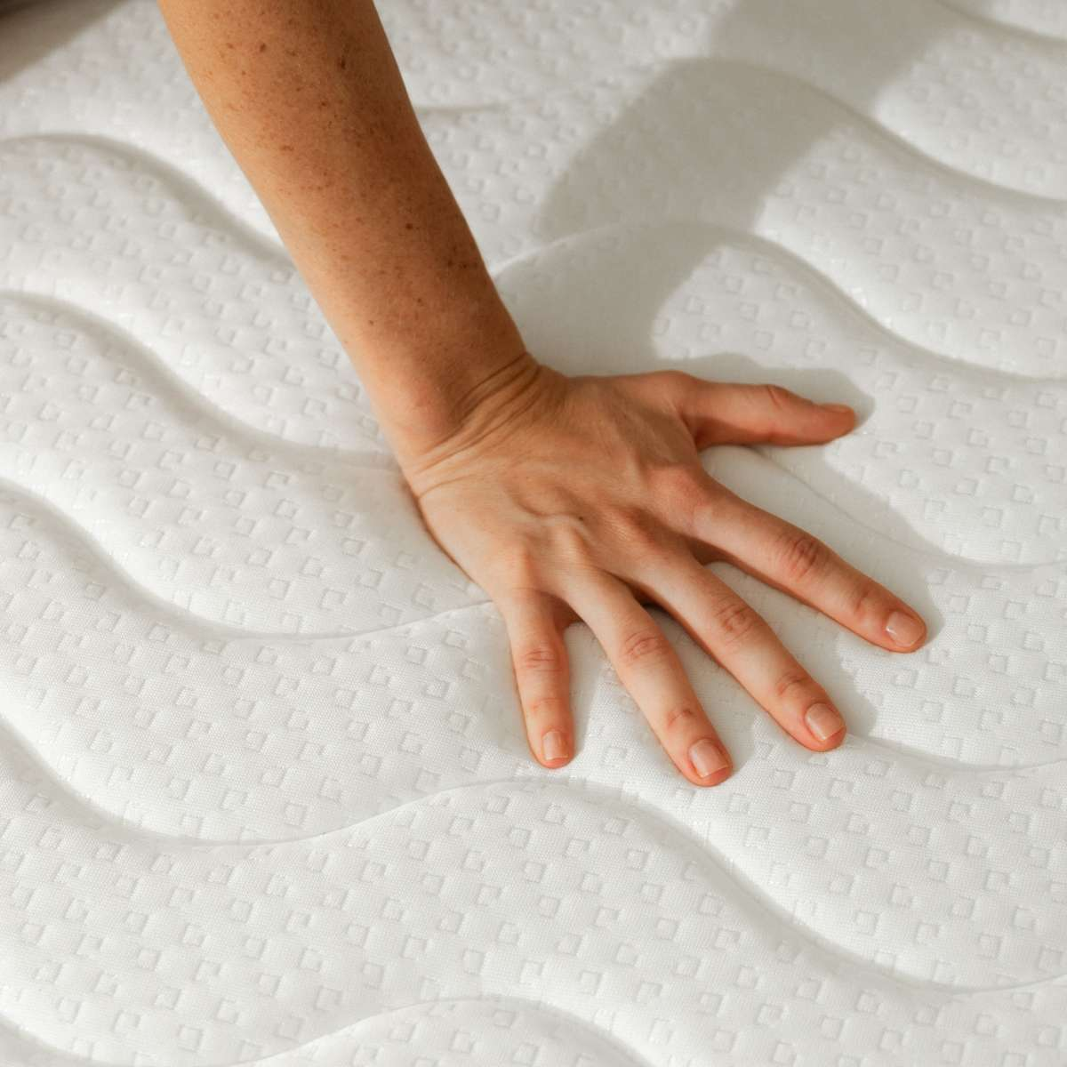 Una mano presiona un colchón blanco y texturizado.