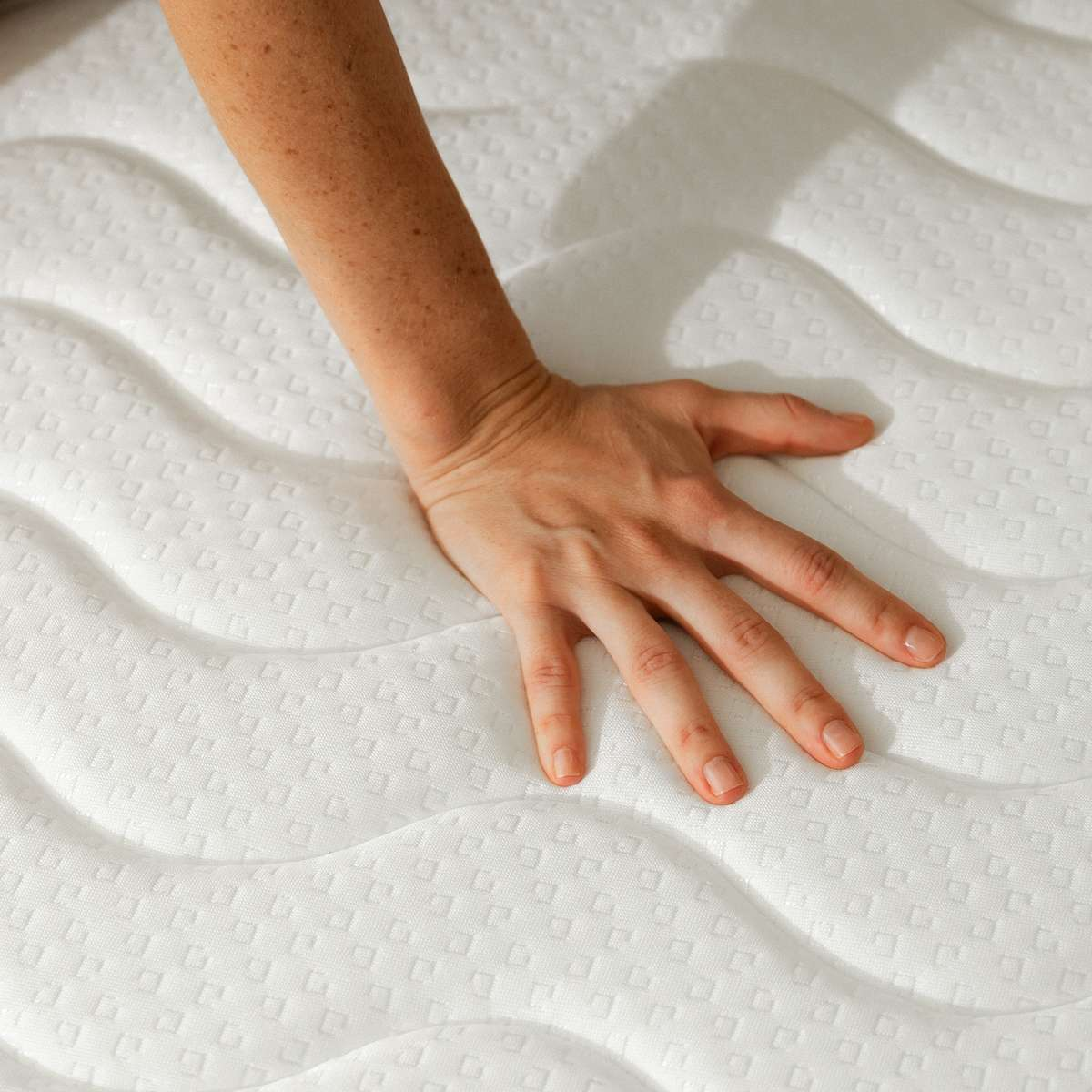 Una mano presiona sobre un colchón blanco y acolchado.