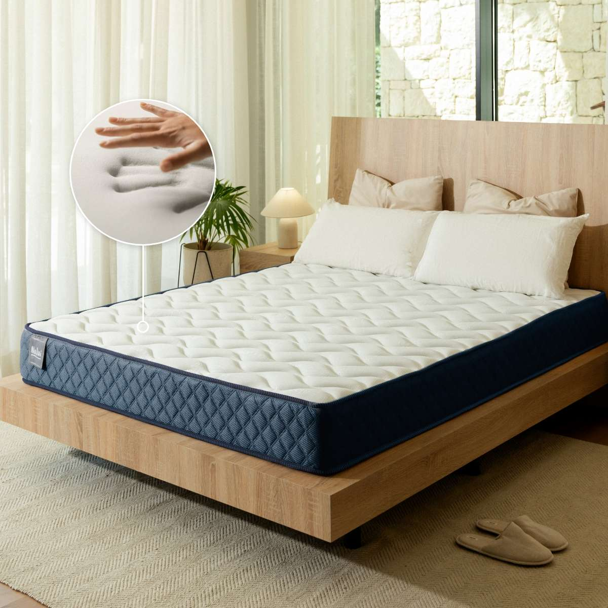 Un colchón blanco y azul con espuma, almohadas y zapatillas en un dormitorio moderno.