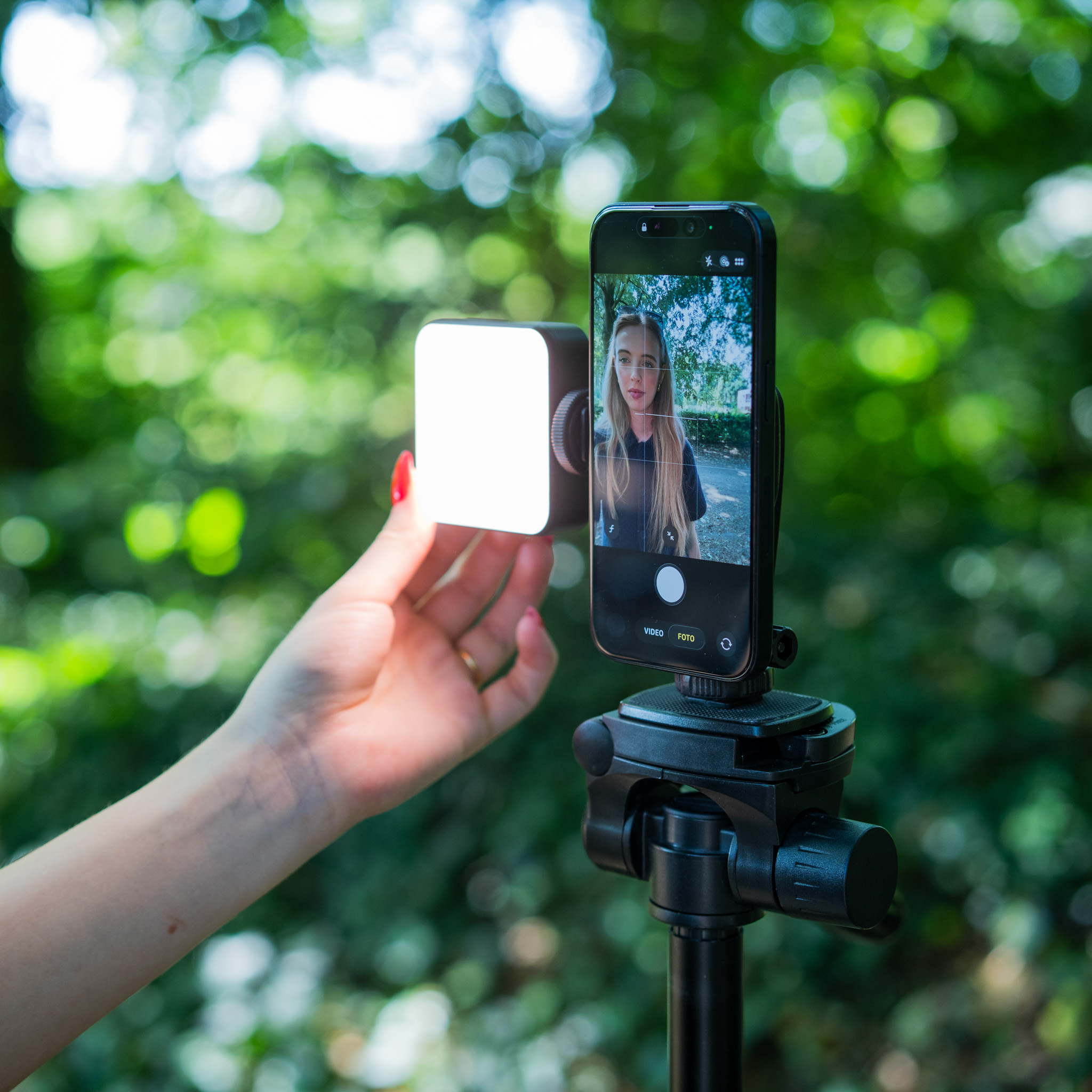Ein Smartphone auf einem Stativ und eine Hand mit einem LED-Licht vor grünem Hintergrund.