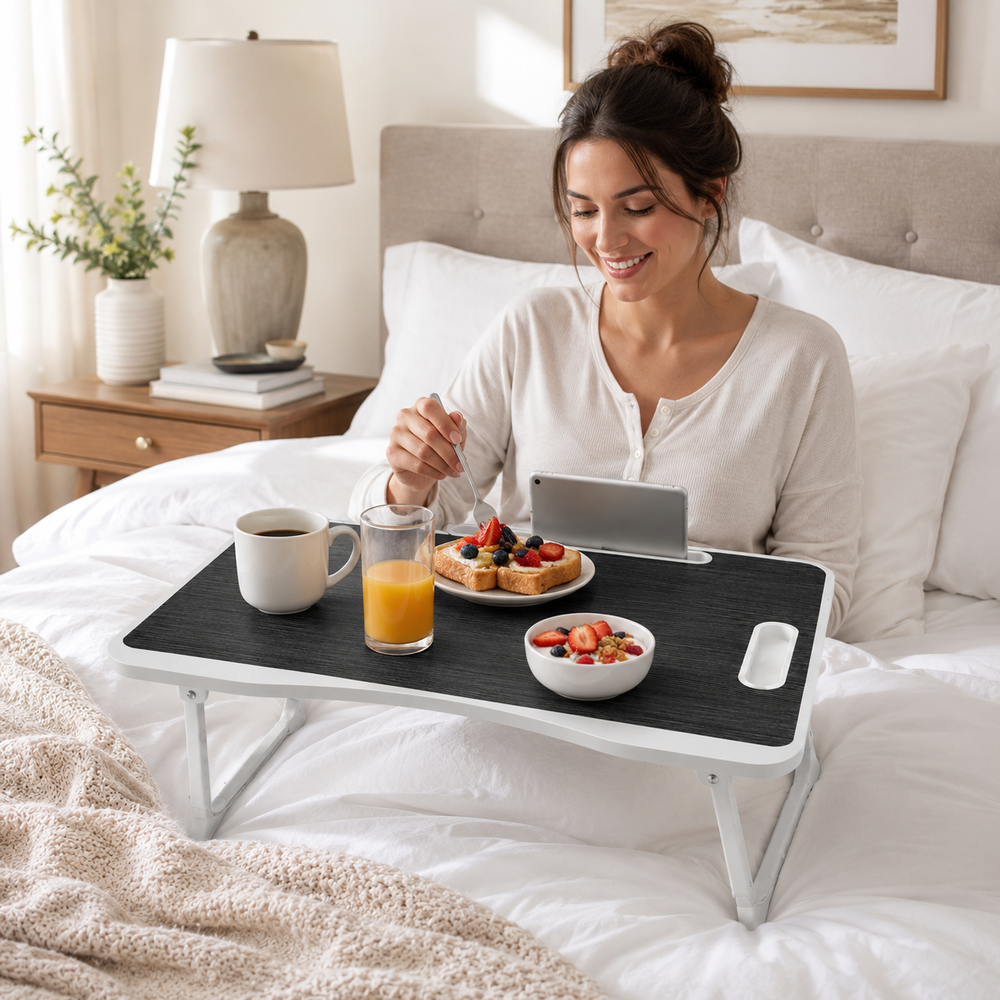 Una mujer en la cama desayuna de una bandeja con tostadas, fruta, jugo y café mientras usa una tableta.
