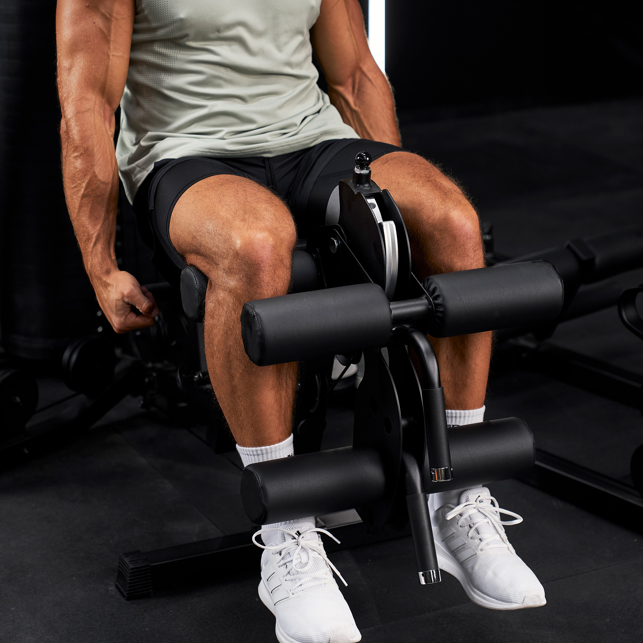 Ein muskulöser Mann sitzt auf einer Beinstreckmaschine in einem Fitnessstudio.