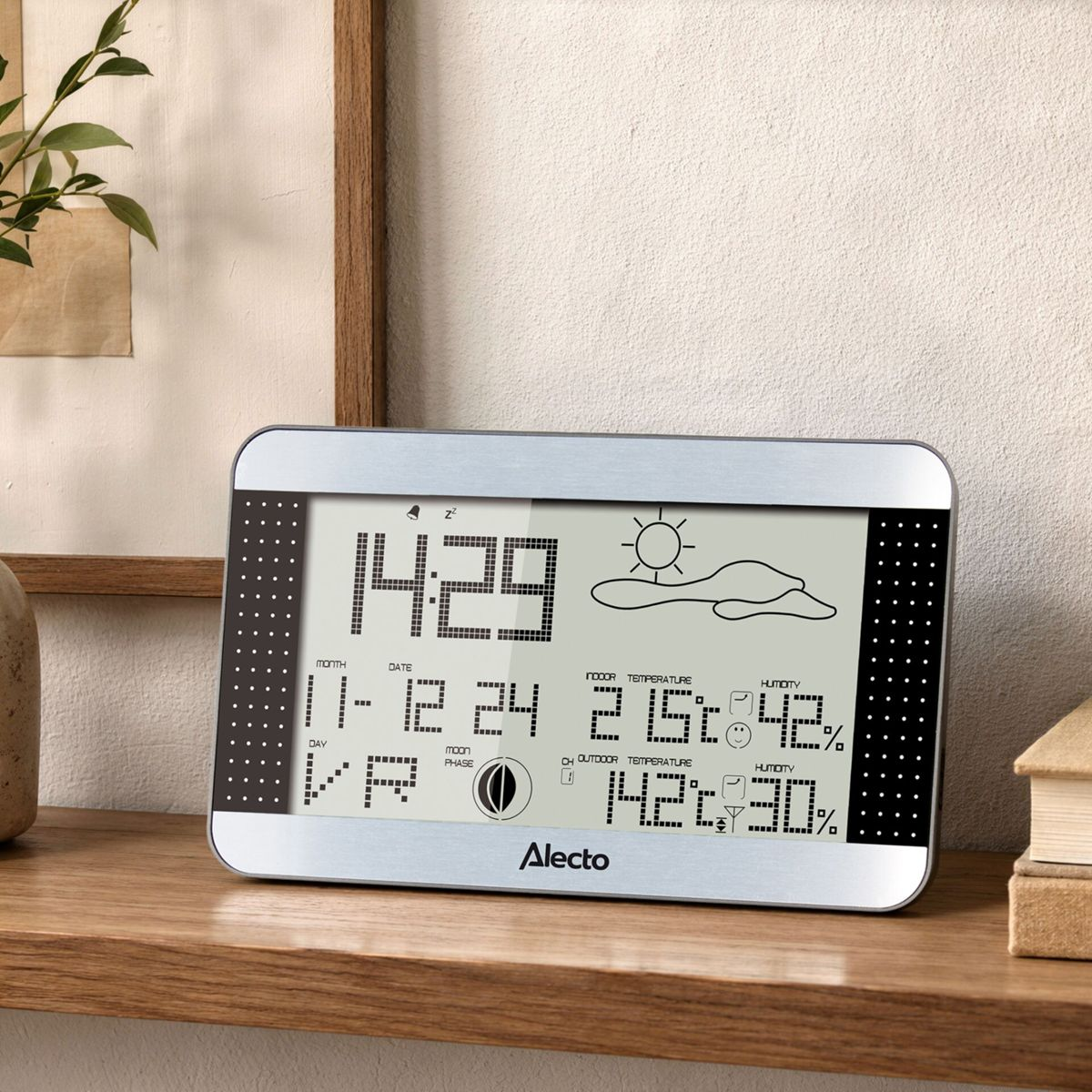 Une horloge station météo numérique sur une étagère en bois affiche l'heure, la date, la température et la météo.