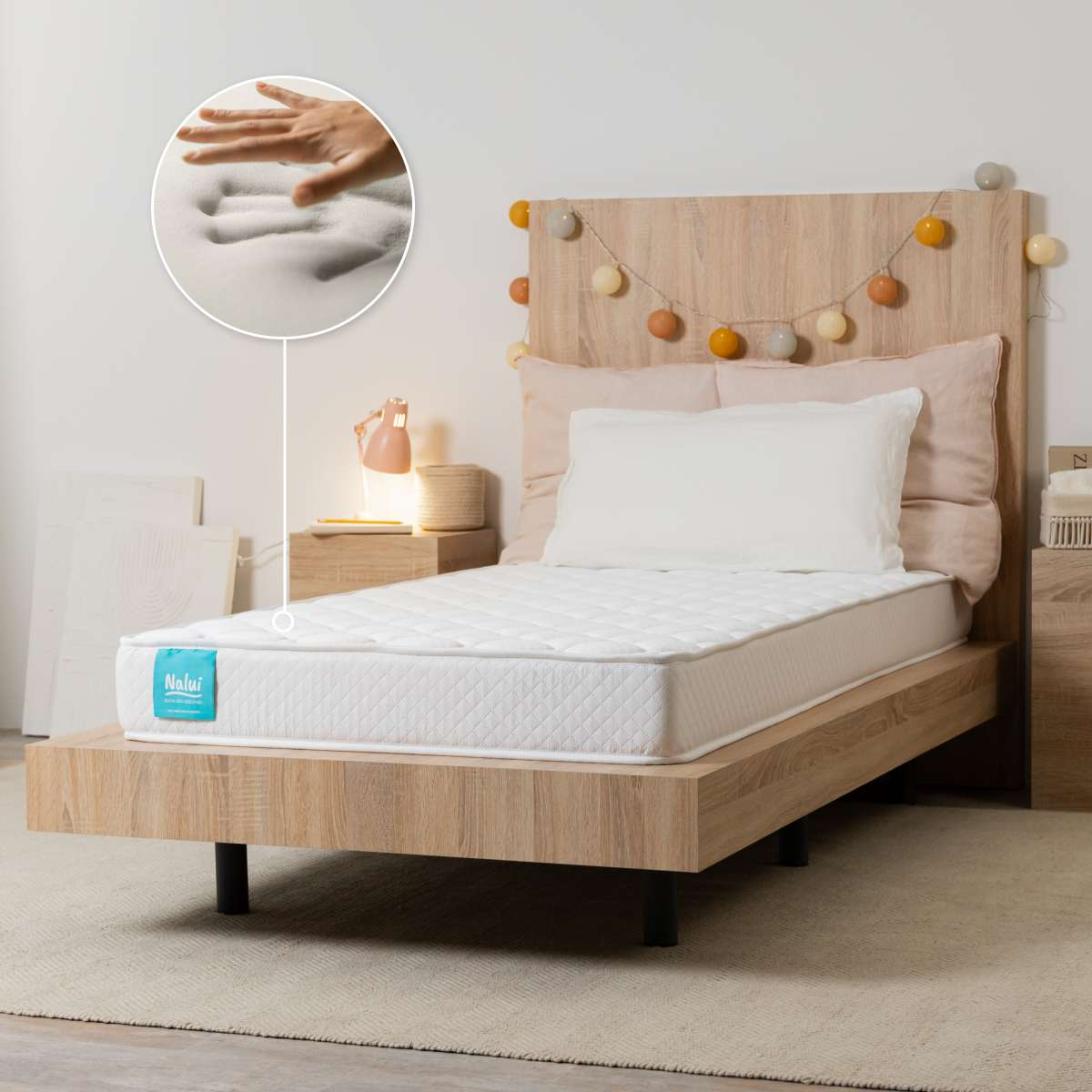 Una cama de madera con colchón blanco. Un inserto muestra una mano presionando la espuma viscoelástica.