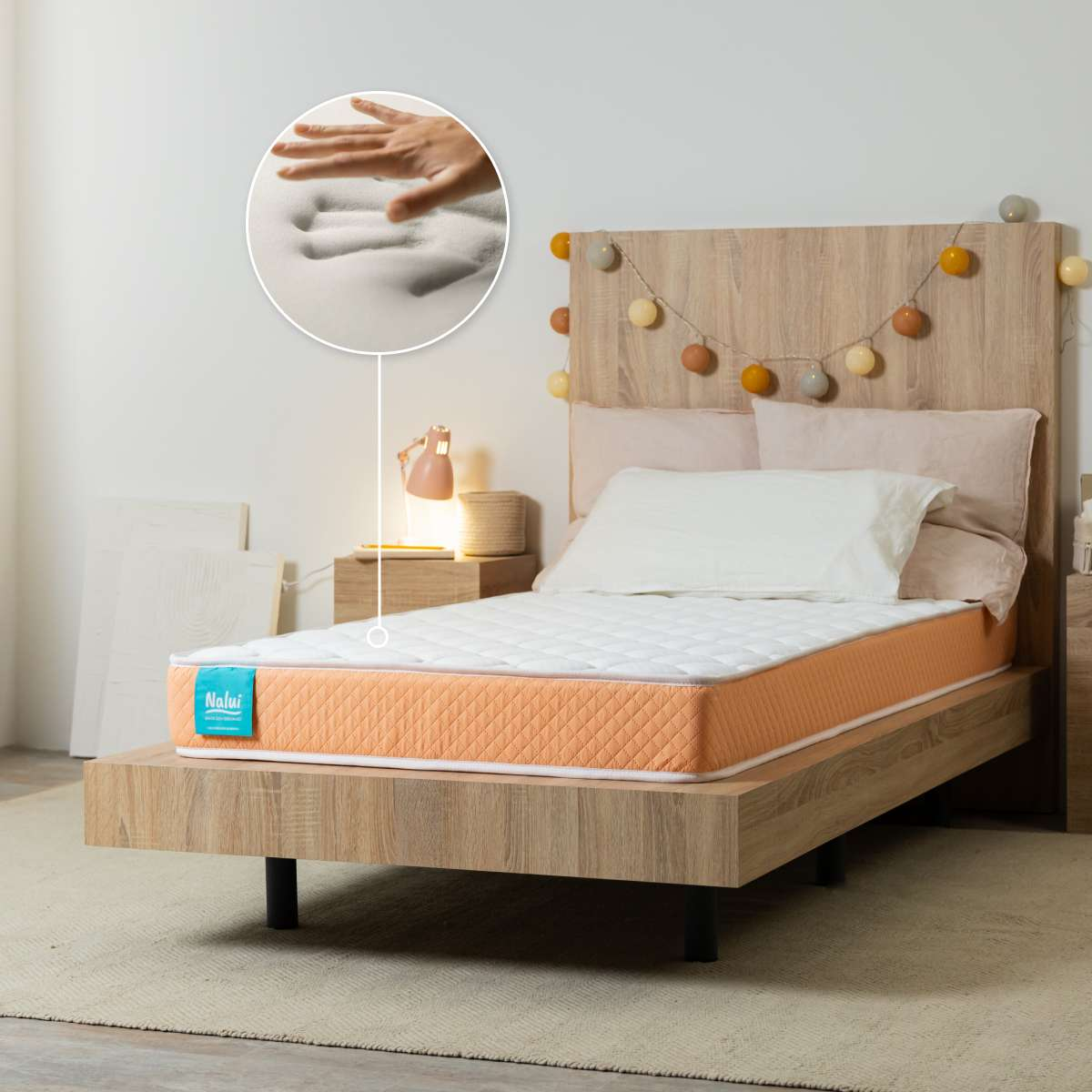 Cama de madera con colchón naranja y blanco, inserto con mano presionando espuma viscoelástica.