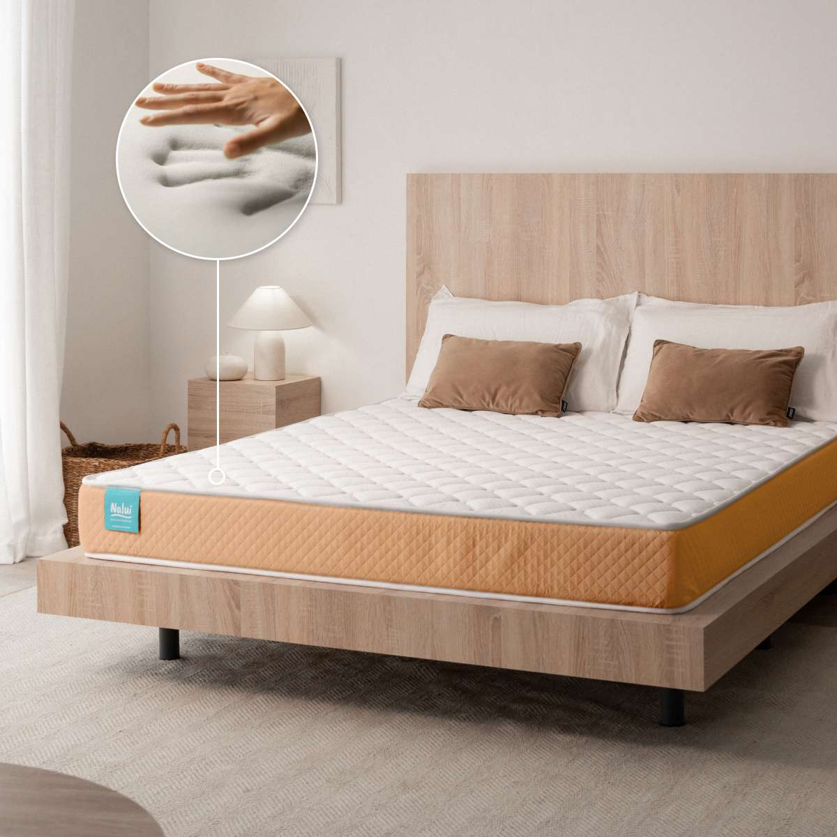 Un colchón blanco y naranja en una cama de madera. Un círculo muestra una mano presionando la espuma suave.