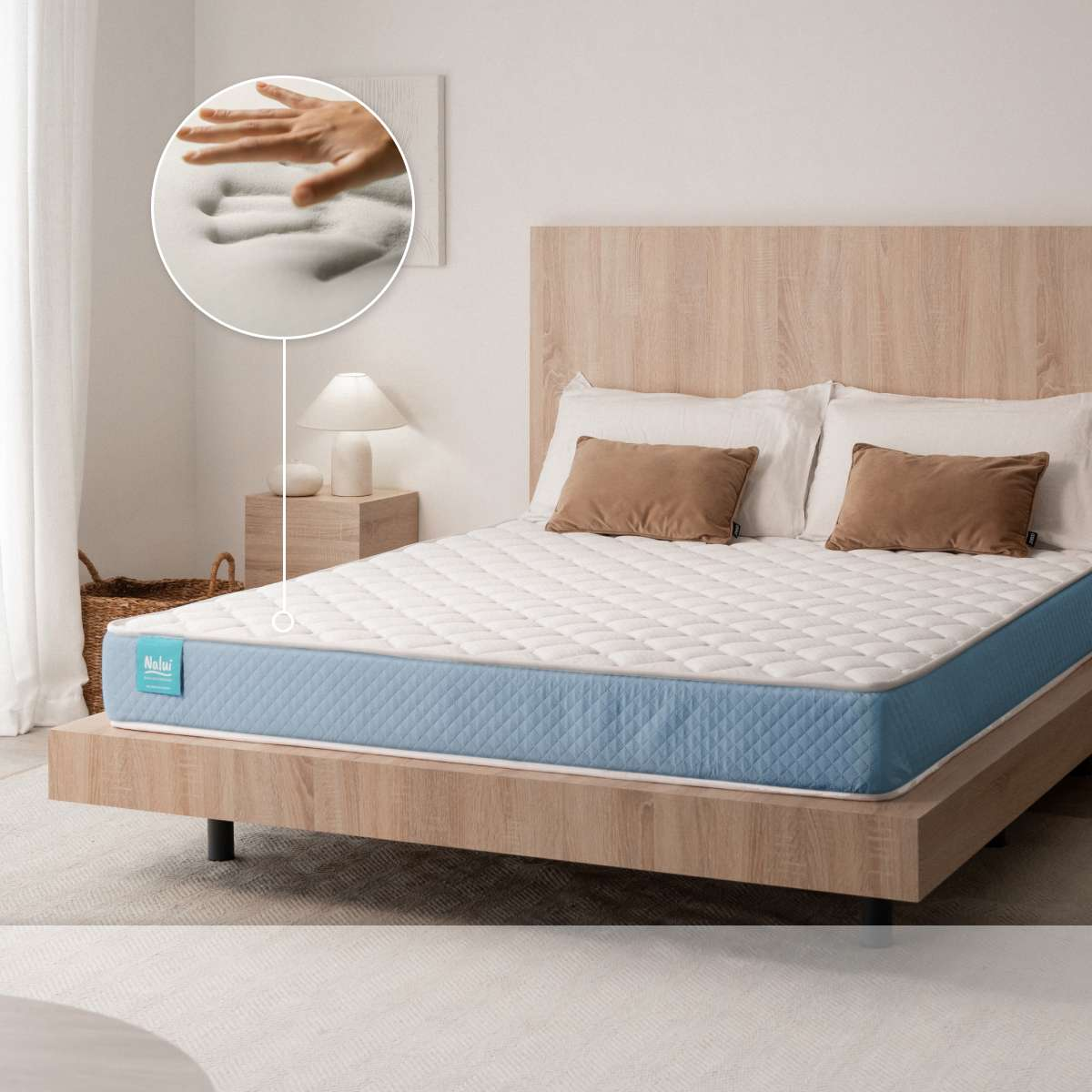 Cama con colchón azul y blanco, con un recuadro circular mostrando una mano presionando la espuma viscoelástica.