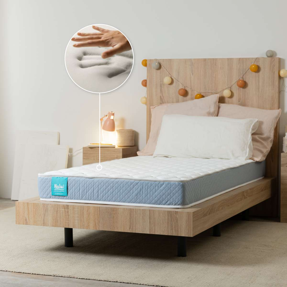 Una cama de madera con colchón y un inserto redondo que muestra una mano presionando la espuma viscoelástica.