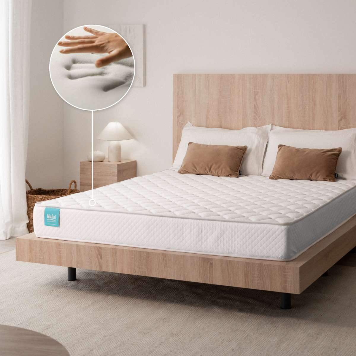 Cama de madera con colchón y almohadas blancas, una mano presionando en un círculo que muestra material suave.