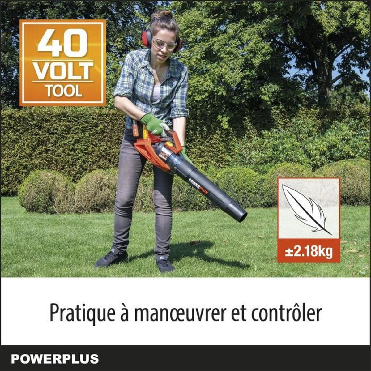 Eine Frau in Schutzkleidung hält einen orangen und schwarzen Laubbläser auf einem grünen Rasen.